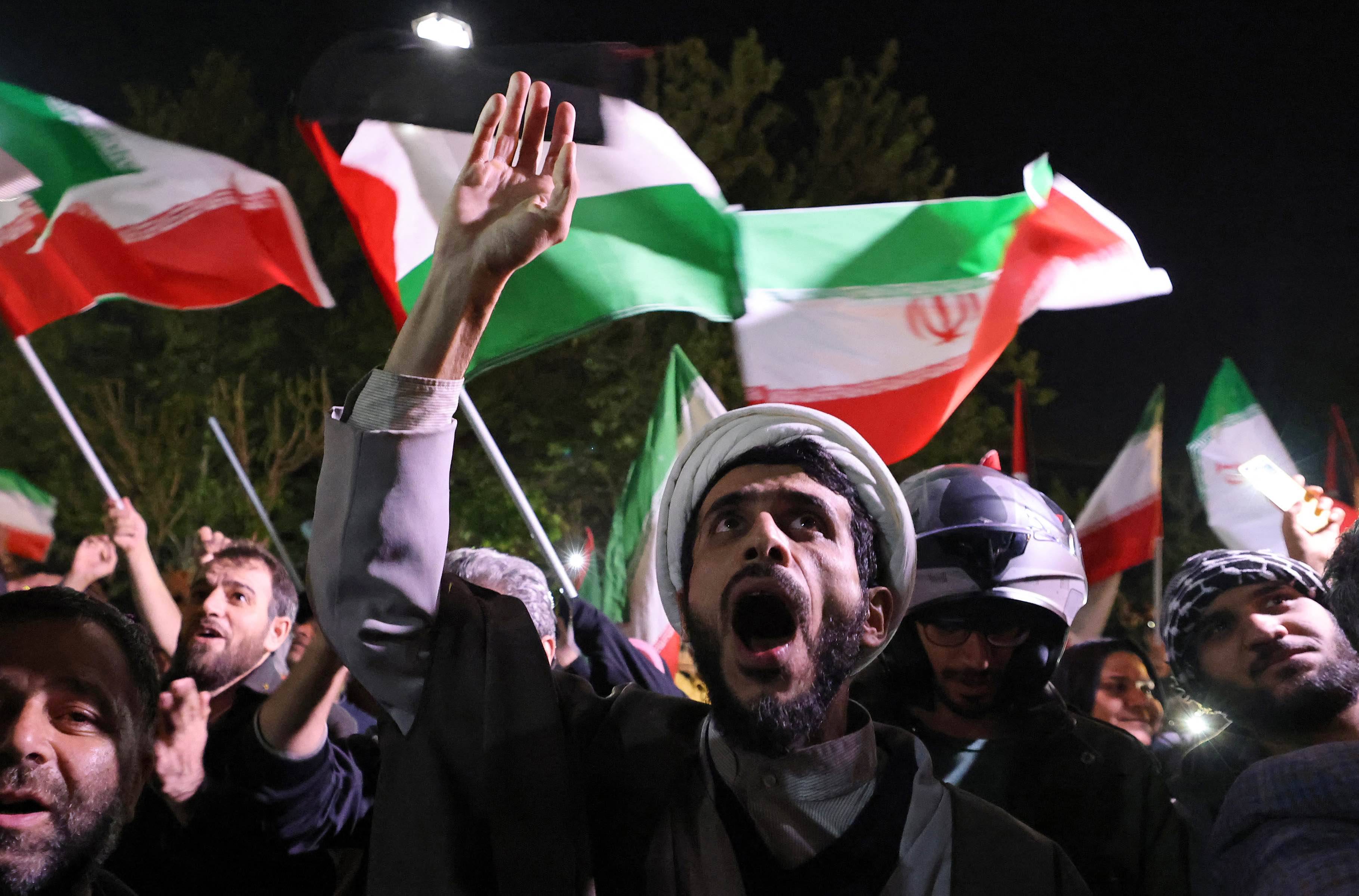 Tłum manifestantów z irańskimi flagami na ulicy w Teheranie przed Ambasadą Brytyjską. Mężczyzna na pierwszy planie wznosi dłoń i krzyczy. Atak Iranu