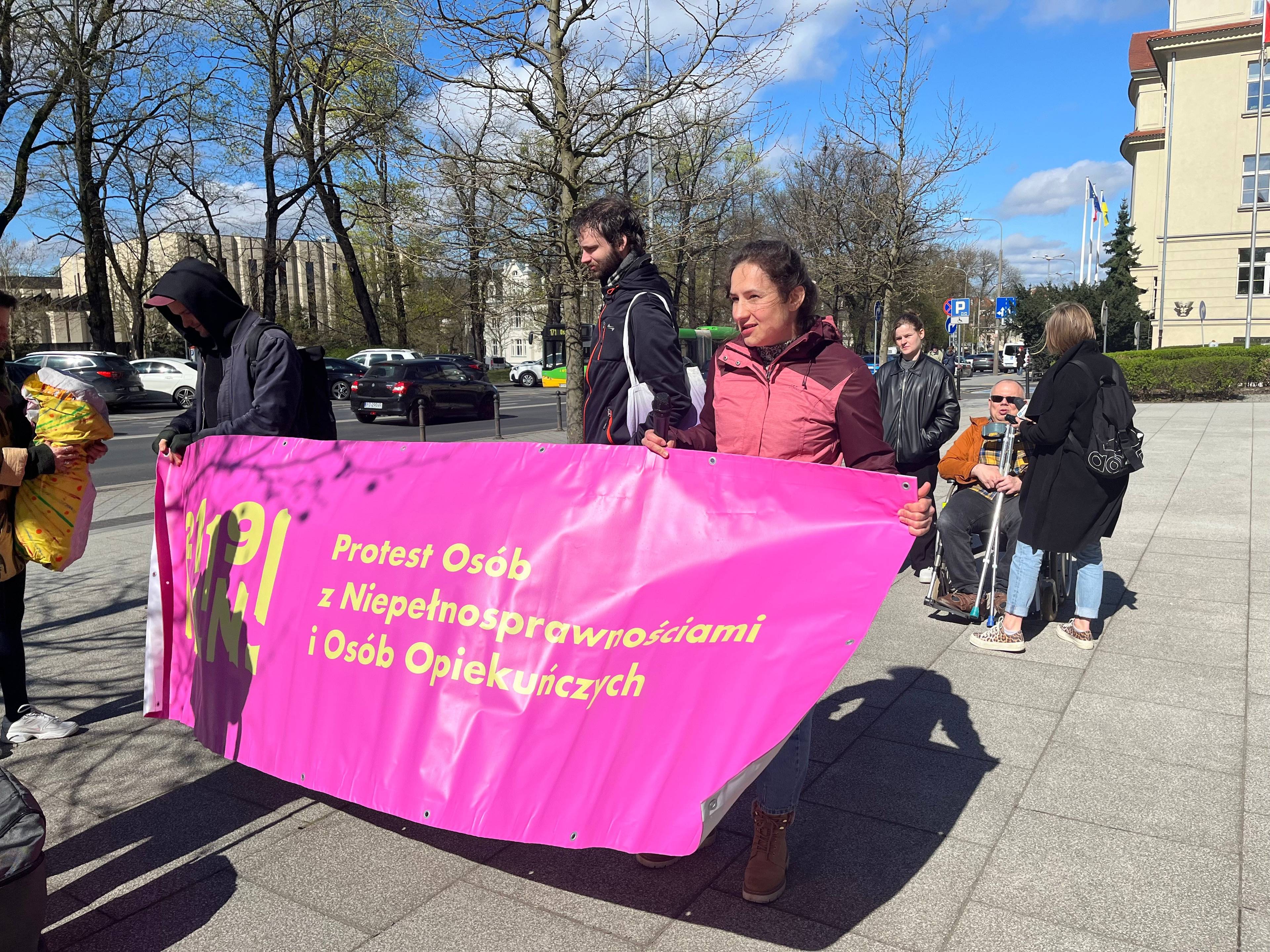 Ludzie z różowym plakatem protestujących osób z niepełnosprawnościami