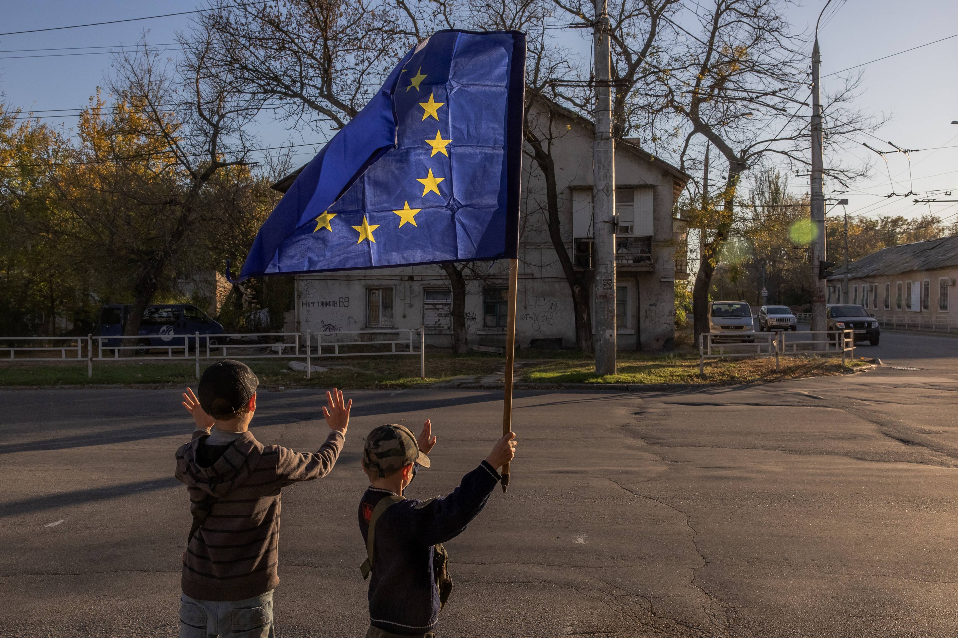 Dwóch chłopców na drodze. Jeden z nich trzyma flagę Unii Europejskiej.