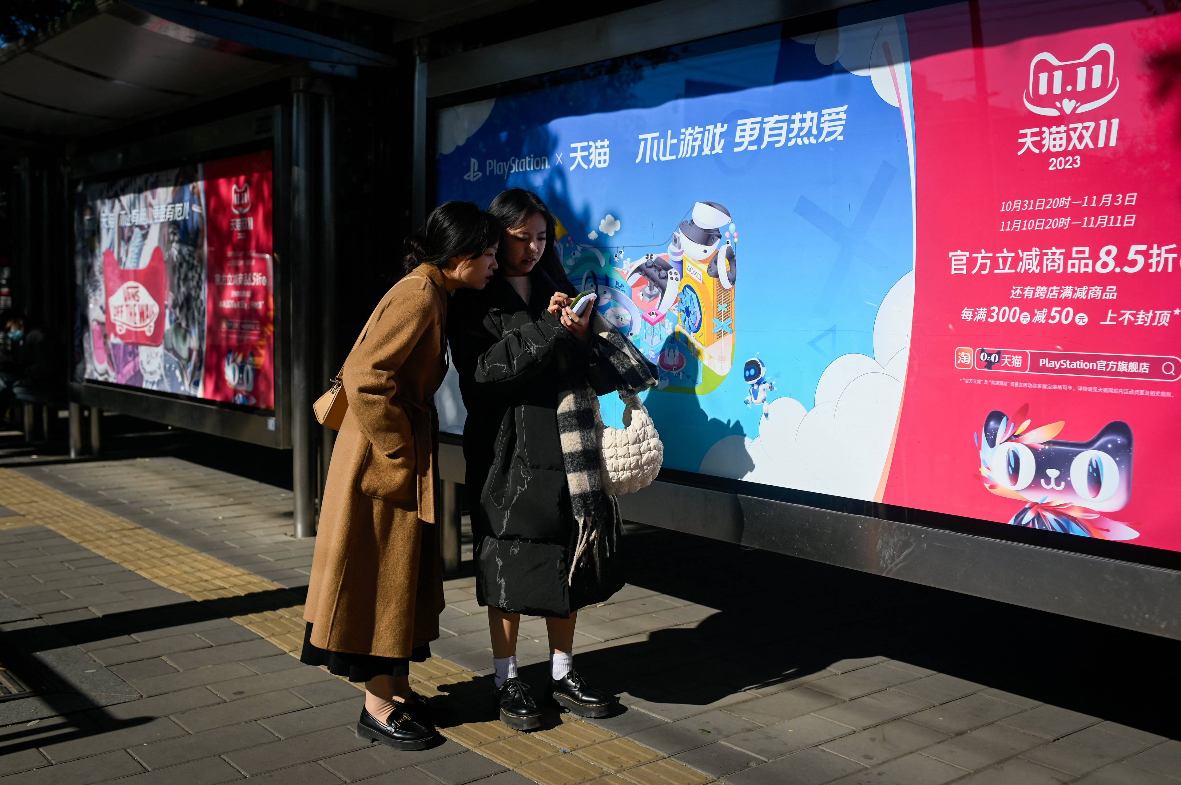 dwie Azjatki sprawdzające coś w komórce, w tle plakat po chińsku