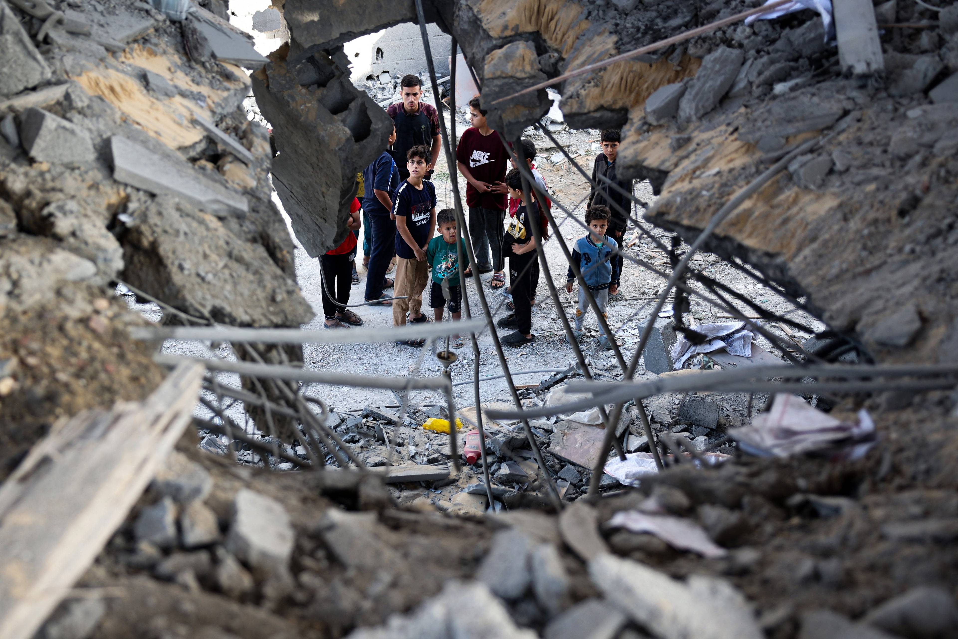 Grupa chłopców i młodych mężczyzn widocznych przez dziurę w ruinach zniszczonego budynku w Rafah na południu Strefy Gazy