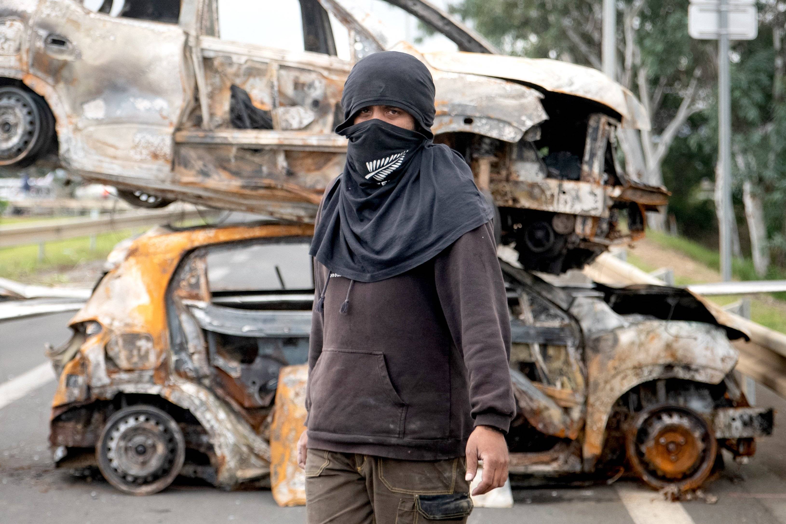 A bystander poses in front of burnt vehicles in a roadblock at the entrance to Ducos, France's Pacific territory of New Caledonia, on May 21, 2024. - The Pacific territory of 270,000 people has been in turmoil since May 13, when violence erupted over French plans to impose new voting rules that would give tens of thousands of non-indigenous residents voting rights.
The unrest has left six people dead, including two police, and hundreds injured. (Photo by Delphine Mayeur / AFP)
