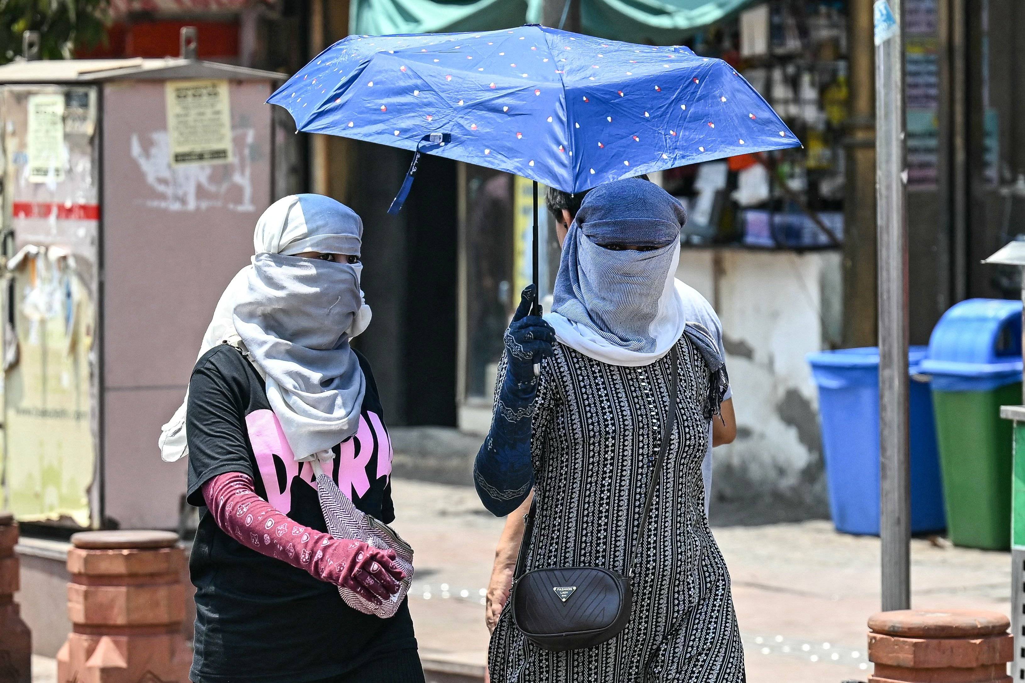 Dwie kobiety na ulicy w Delhi pod parasolem zakrywają całe ciało przed ekstremalnym upałem