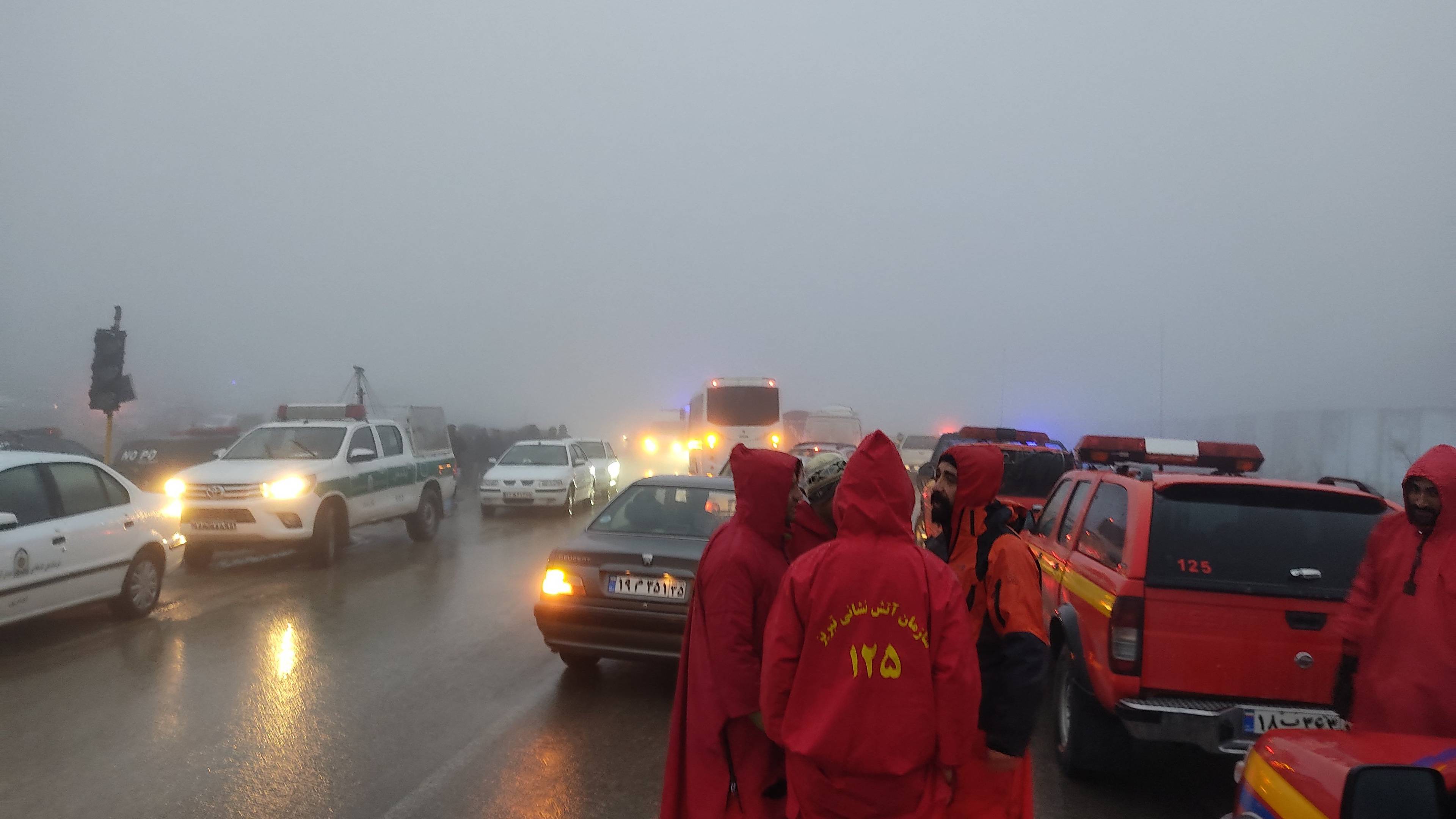 Ratownicy w czerwonych kurtkach stoją na drodze we mgle. w tle widać samochody terenowe