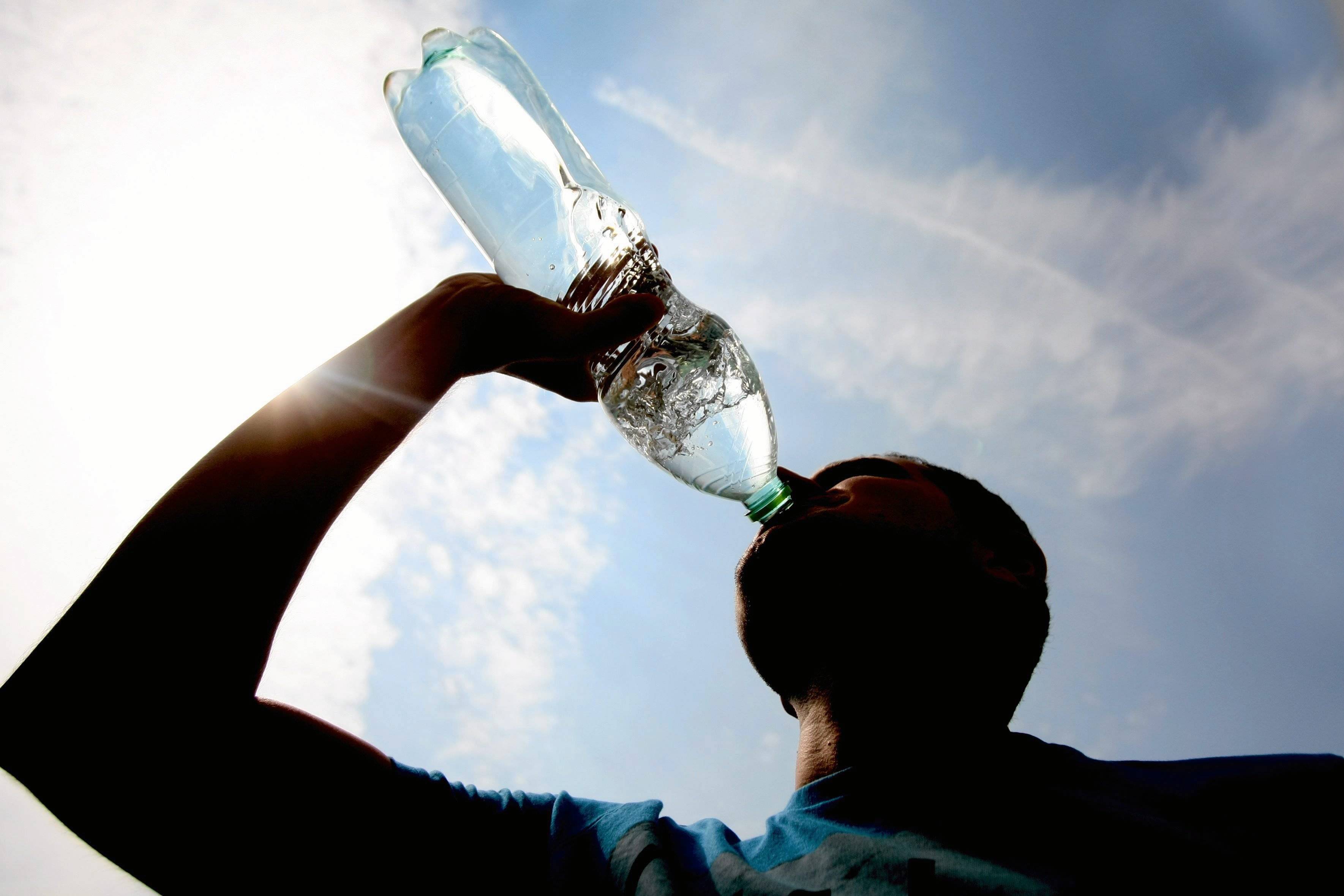 Mężczyzna pije wodę z butelki na tle rozżarzonego gorącego dnia
