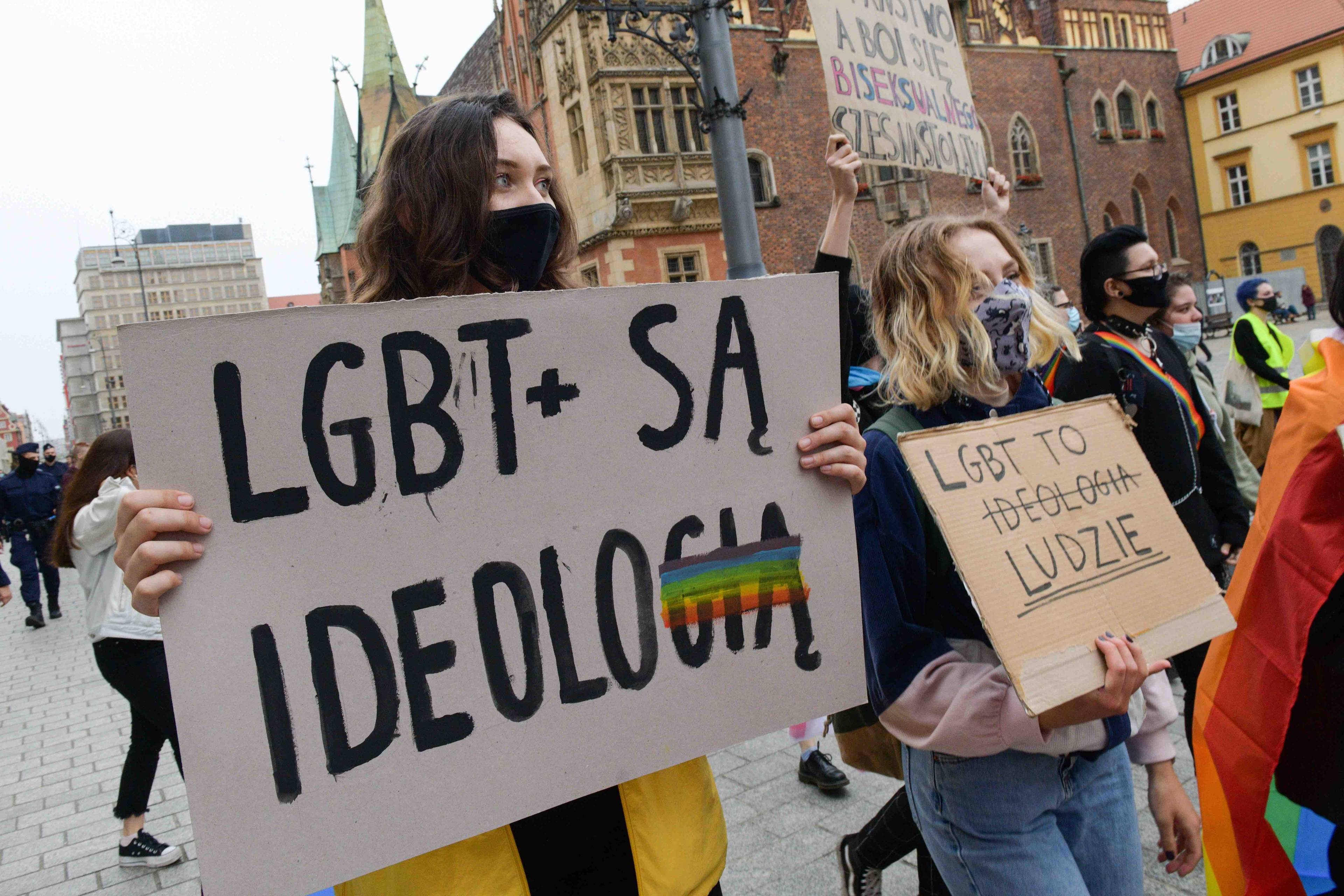 Demonstracja przeciwko atakom na społeczność LGBT, na pierwszym planie dziewczyna trzyma plakat z napisem LGBT+ to ideologia gdzie ostatnie litery słowa ideologia są skreślone, Obok inna osoba niesie plakat z napisem LGBT to ludzie. Wolność słowa