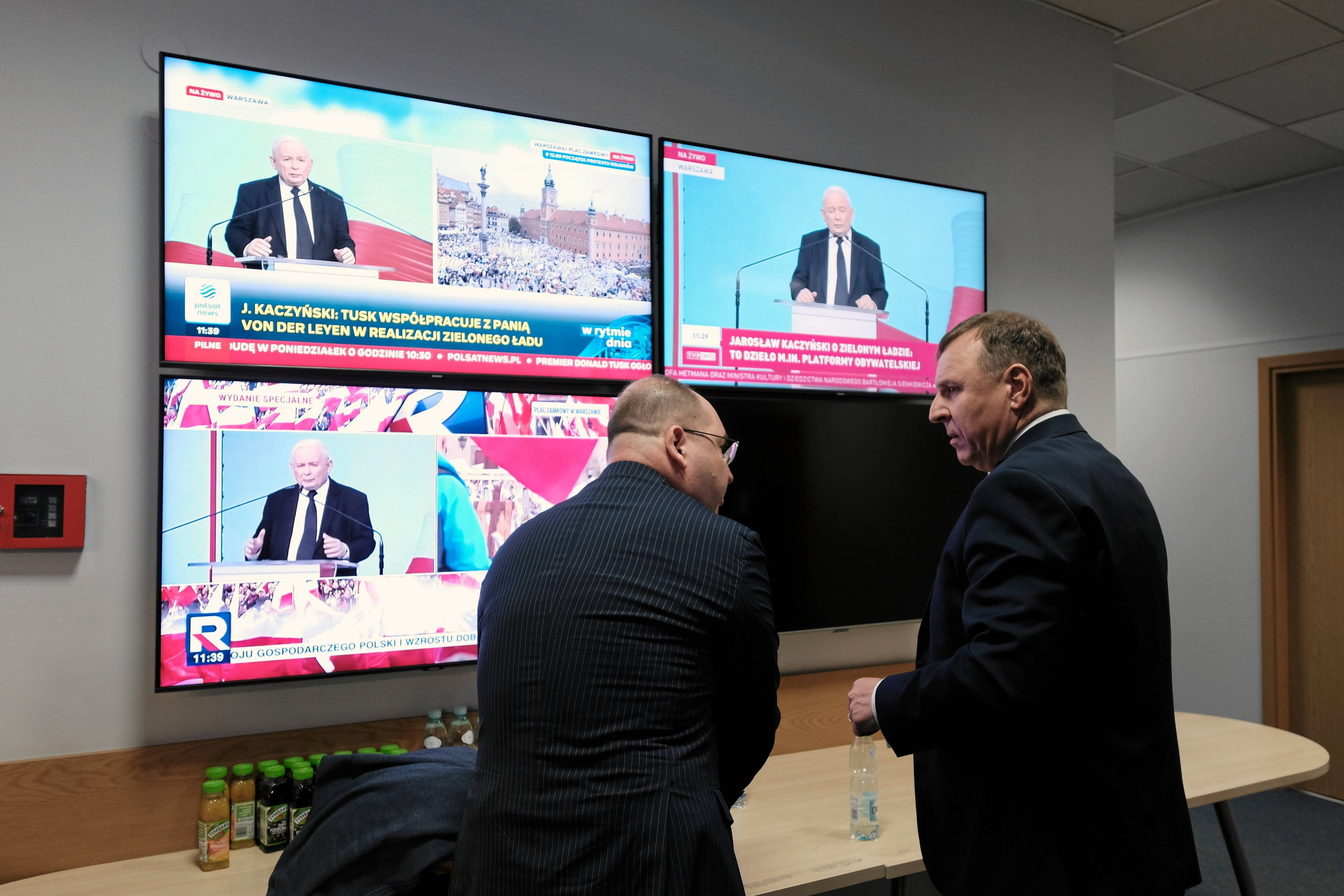 Adam Bielan i Jacek Kurski na tle trzech ekranów, na których widać Jarosława Kaczyńskiego