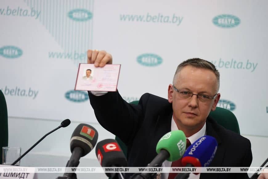 Tomasz Szmydt w wyciągniętej dłoni trzyma dokument wyglądający na legitymację