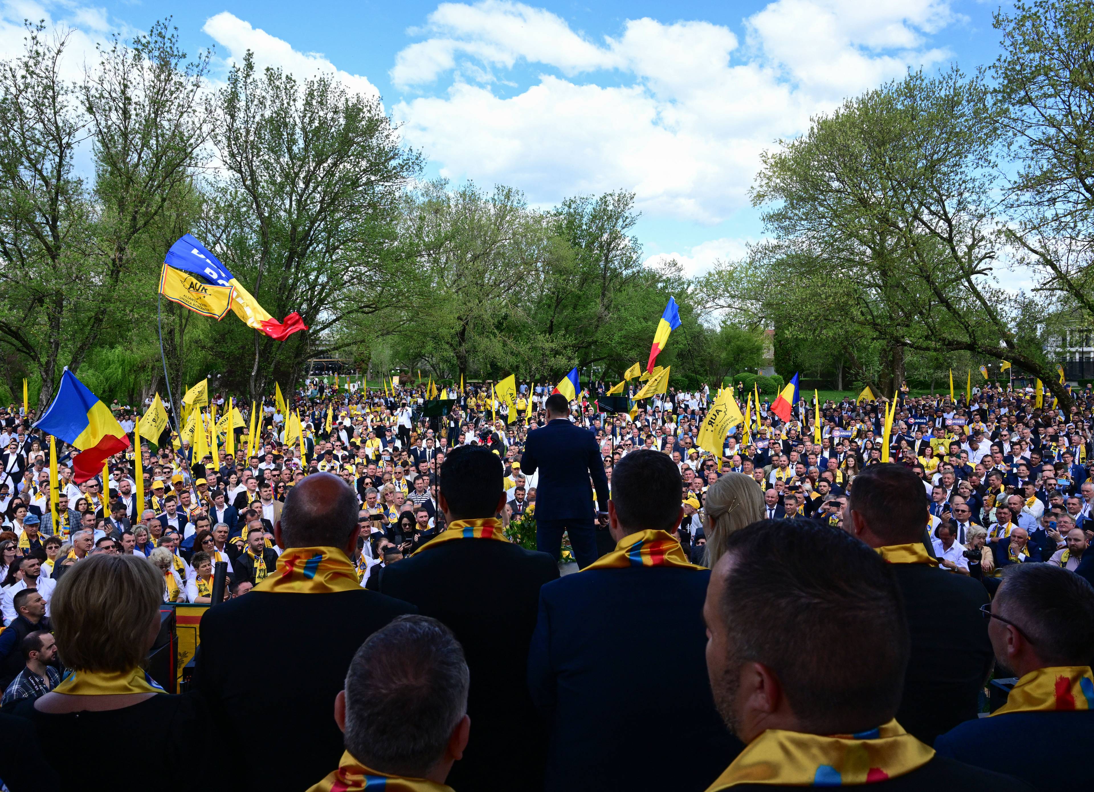 Wiec polityczny przed wyborami w Rumuni, lider stoi tyłem do obiektywu, przed nim tłum z rumuńskimi flagami