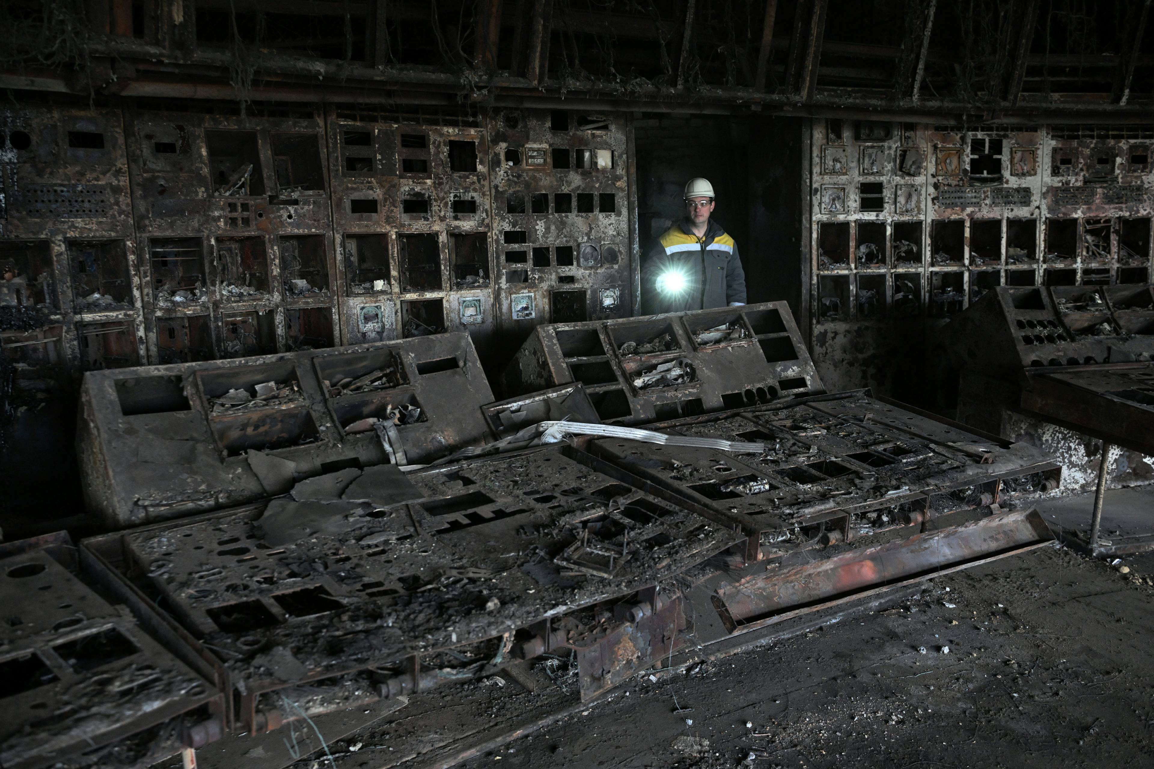 Na zdjęciu widać pracownika elektrowni, który przechodzi przez spalone pomieszczenie. W ręce trzyma włączoną latarkę. Ukraińska energetyka zagrożona