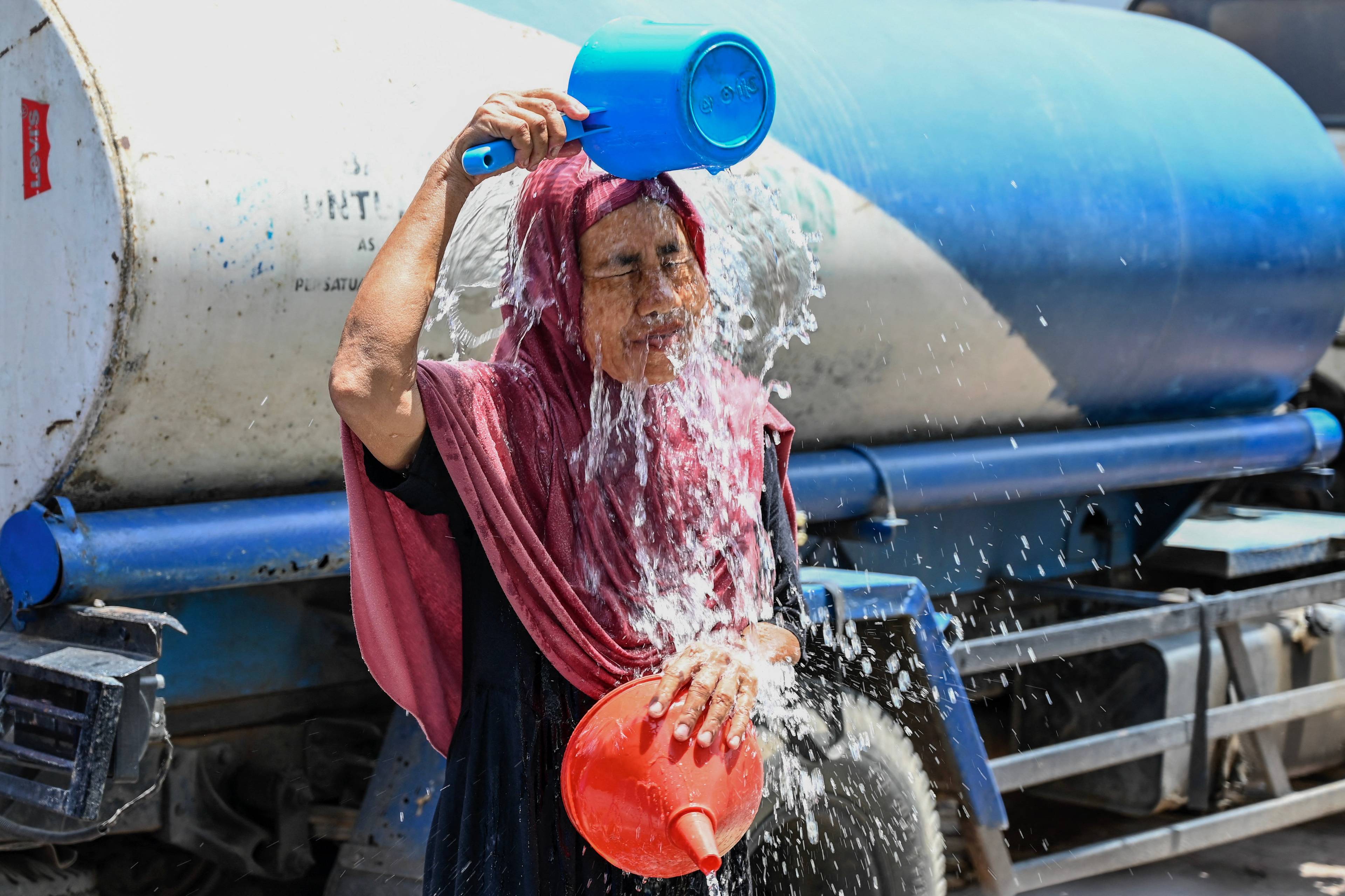 Kobieta w chuście chłodzi się z wiadra wypełnionego wodą