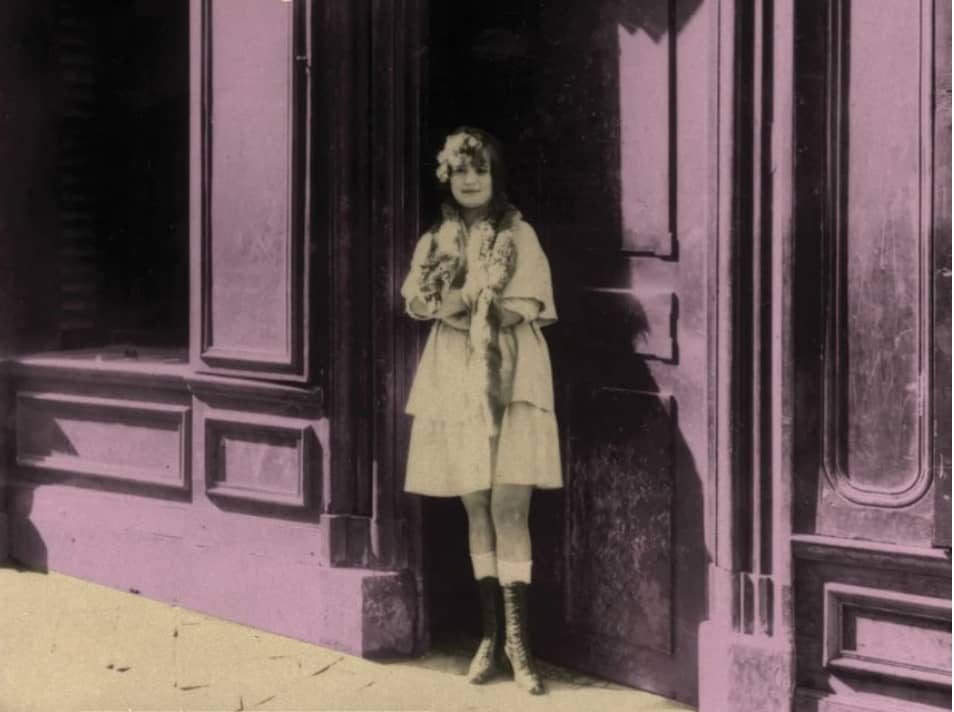 Młoda dziewczyna stoi na ulicy przed wejściem do kamienicy.