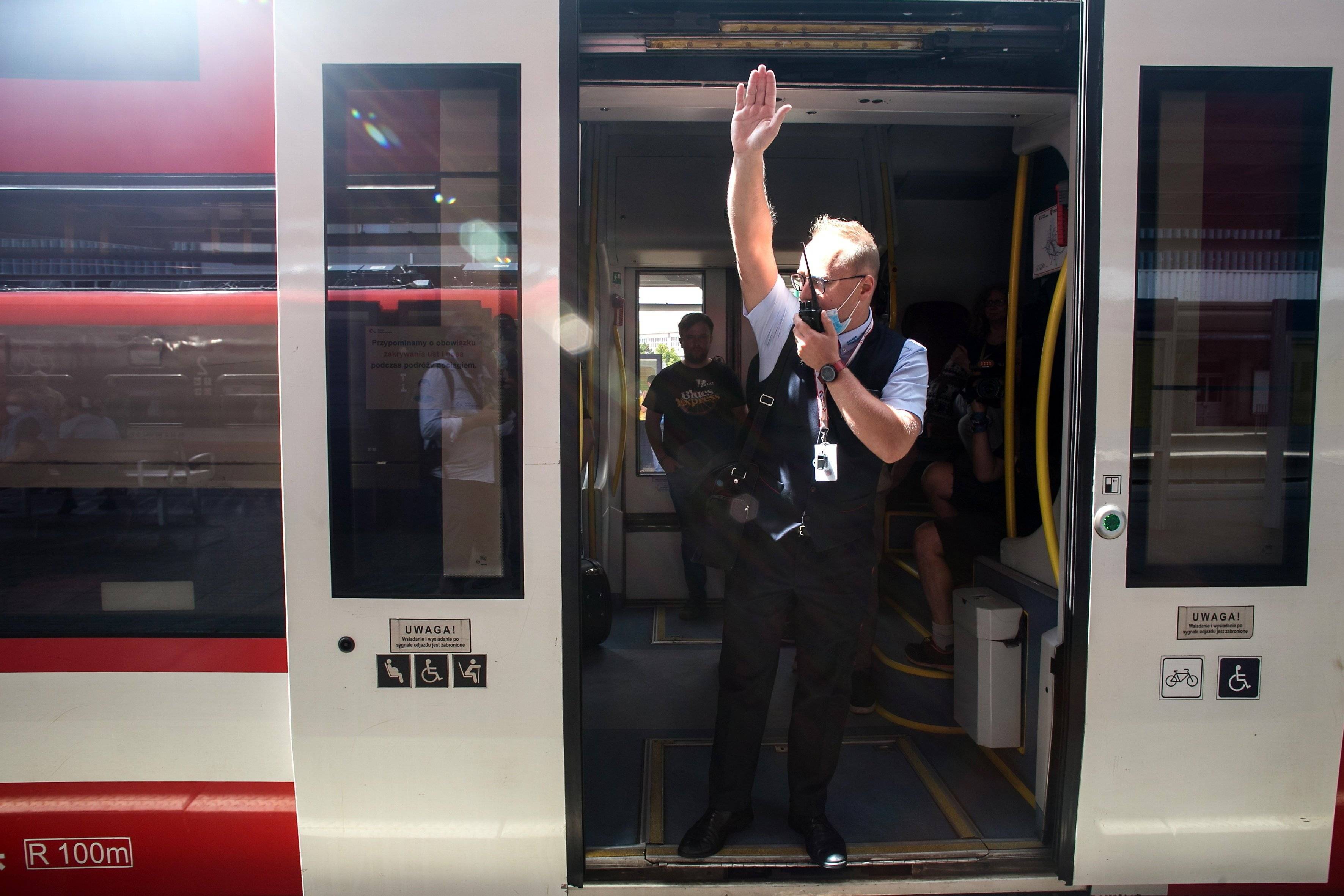 konduktor z krótkofalówką i wyciągniętą ręką ogłasza odjazd w drzwiach pociągu