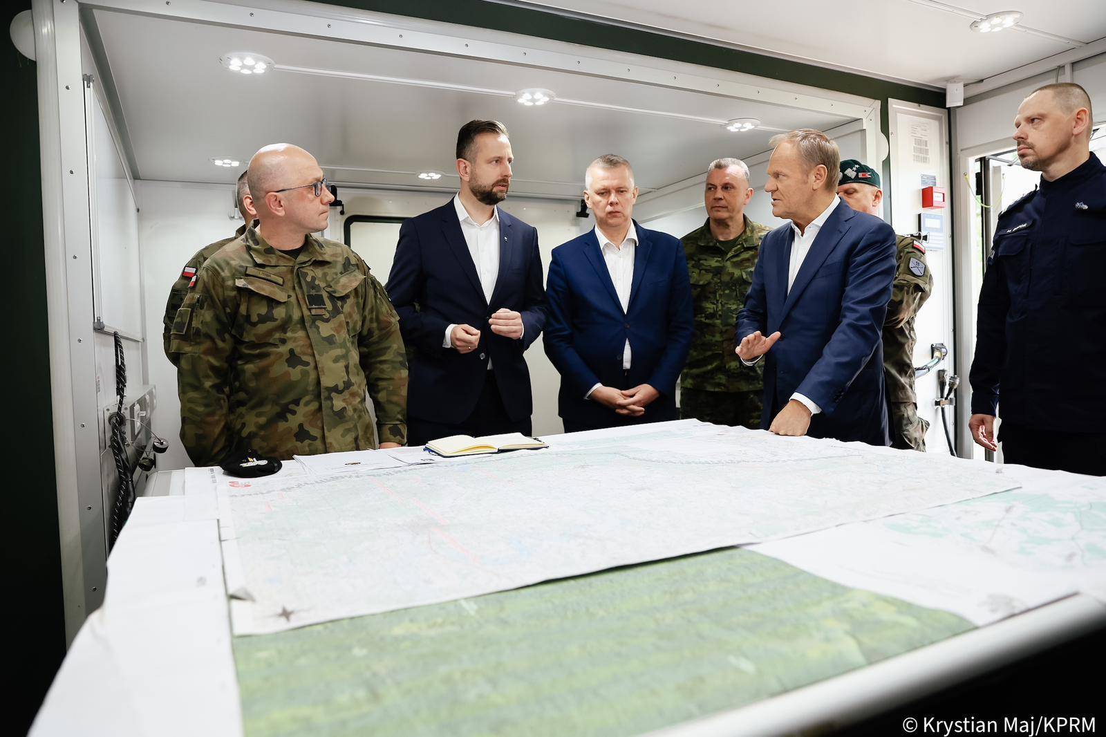 Politycy w marynarkach i wojskowi w mundurach rozmawiają nad mapą sztabową położoną na stole