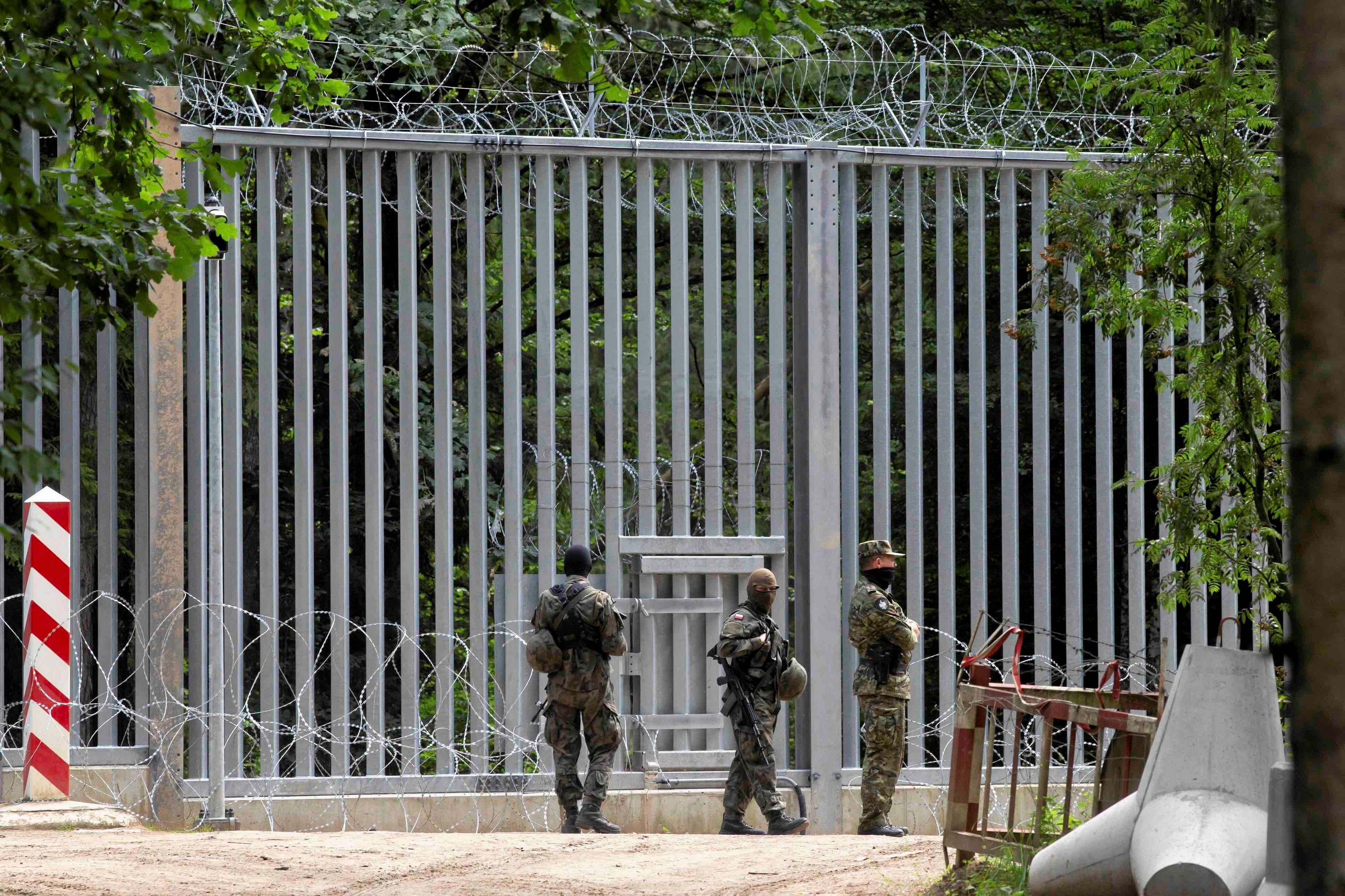 żołnierze stoją przed płotem granicznym, z lewej strony widać biało-czerwony słupek graniczny