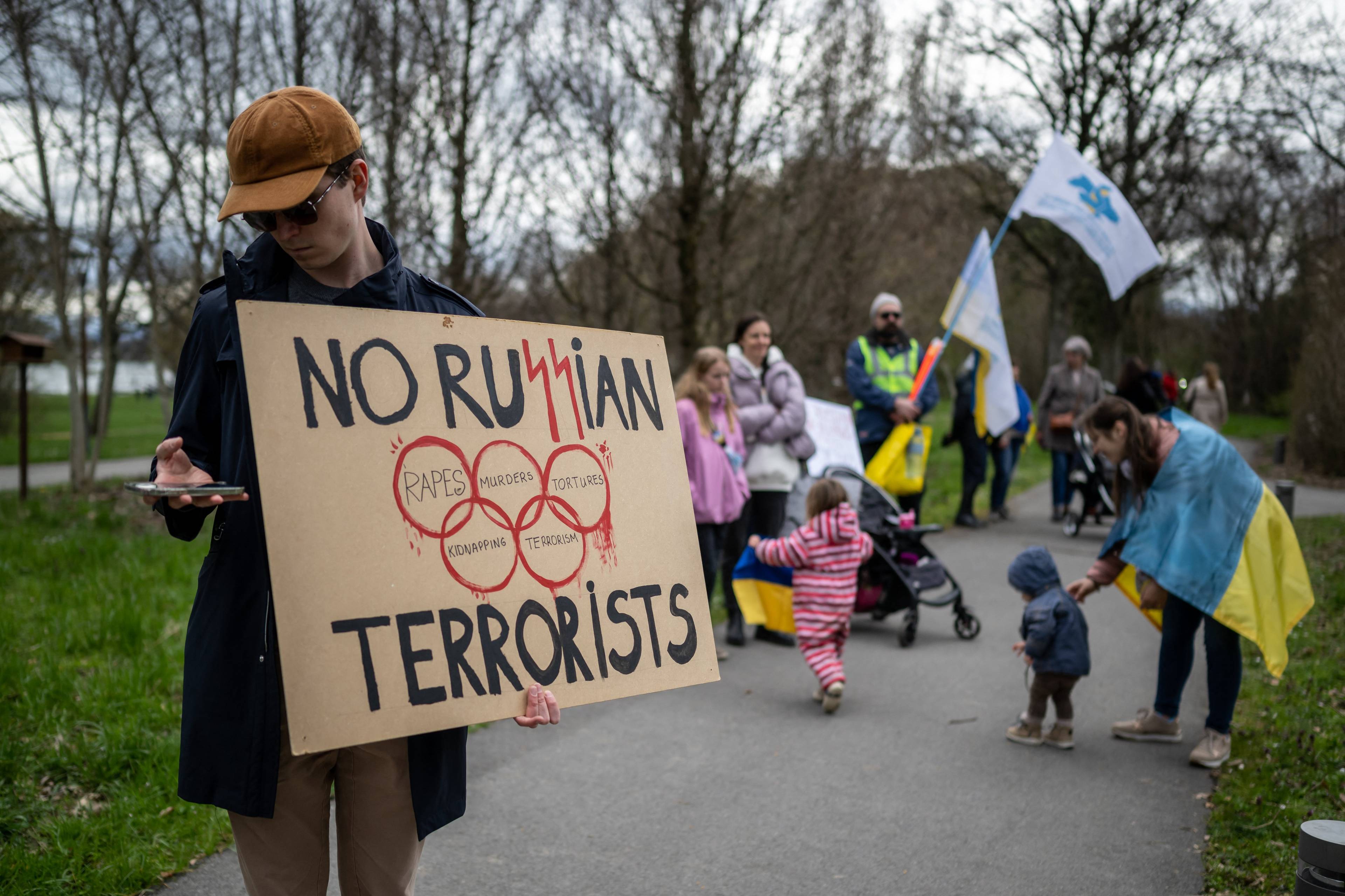 Demonstranci trzymają transparent: No ru$$ian terrorist" ze znakiem kół olimpijskich