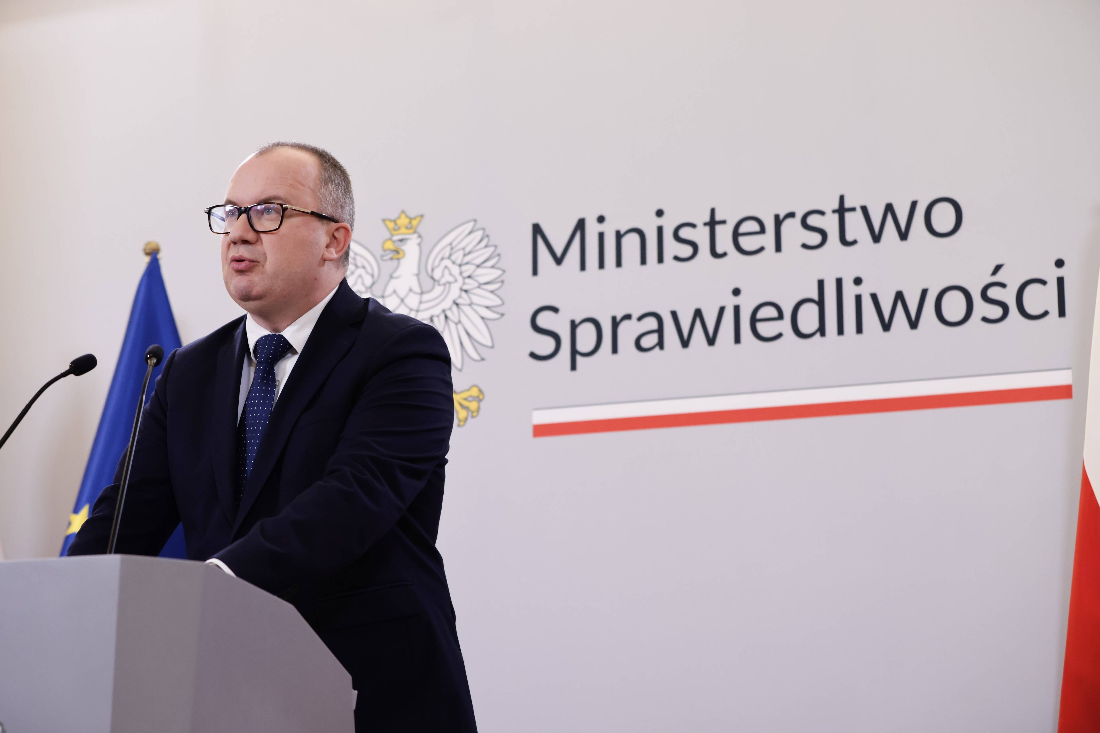 Mężczyzna przemawia na tle logo ministerstwa sprawiedliwości