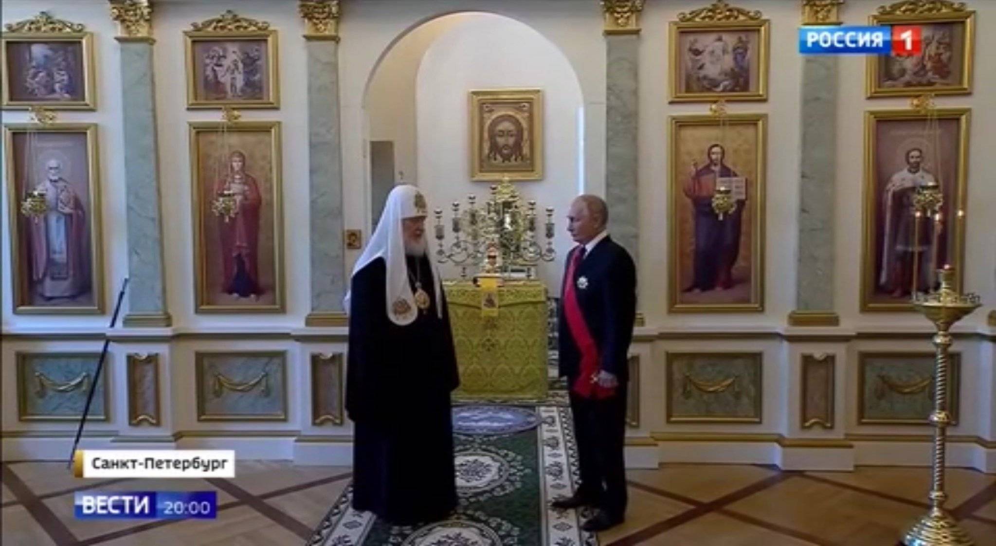 Putin i patriaracha w białym welonie i czarnej szacie. Putin ma order z czerwoną szarfą. Na ścianie - dużo ikon
