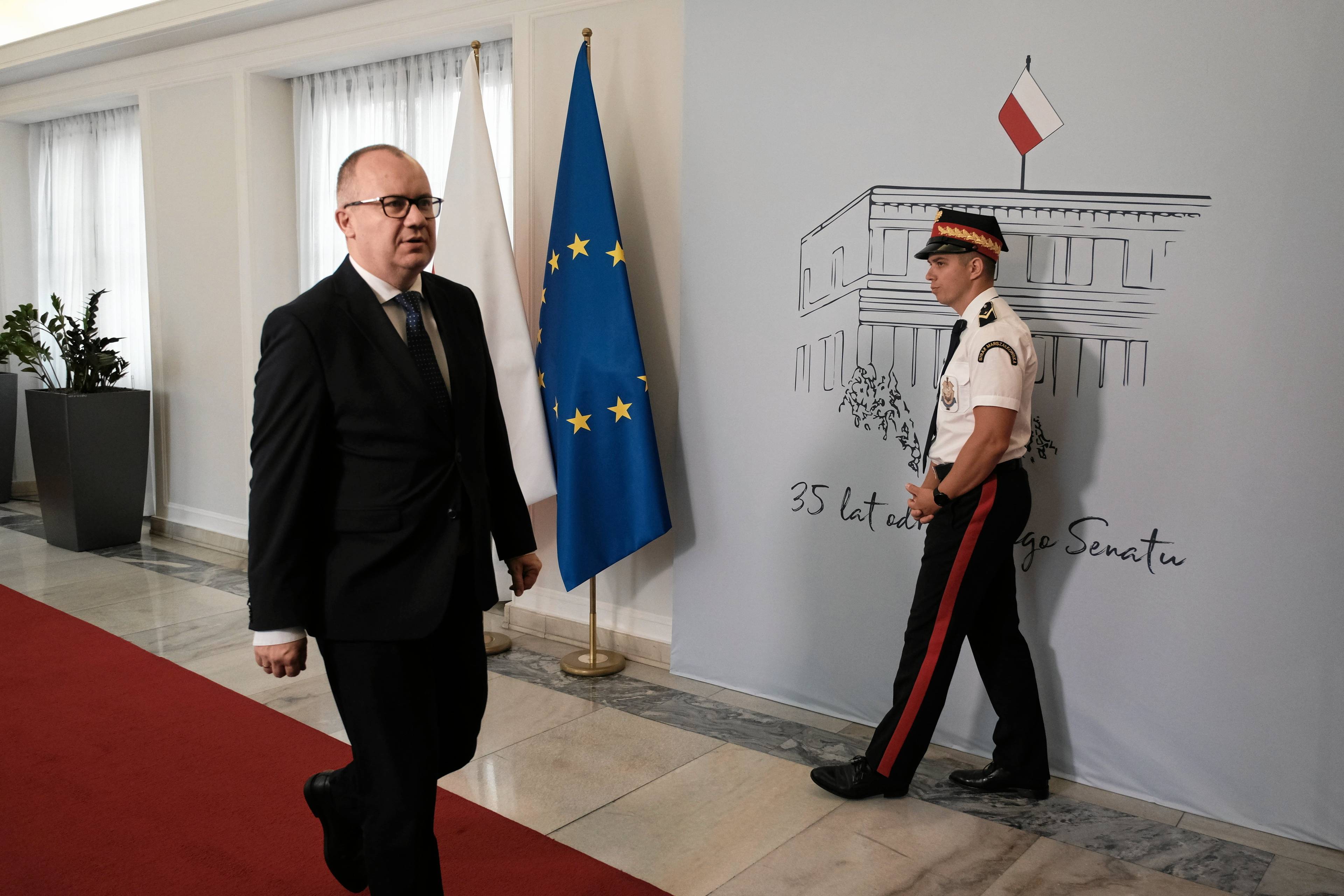 Adam Bodnar idzie korytarzem w parlamencie, obok stoi stoi strażnik