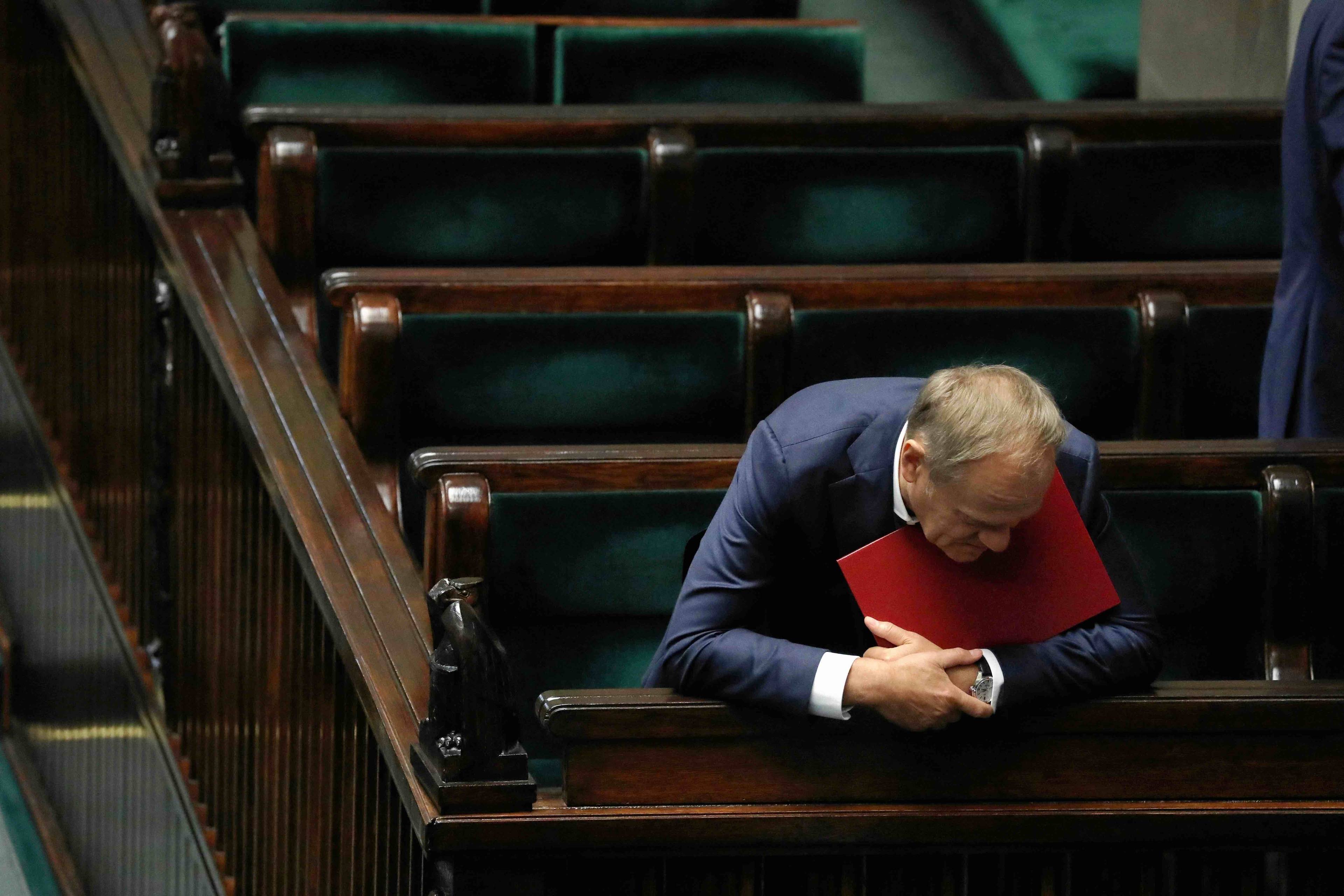 Donald Tusk wychyla się z ław rządowych w Sejmie, trzymając pod brodą czerwoną teczkę. Ustawa dekryminalizacyjna