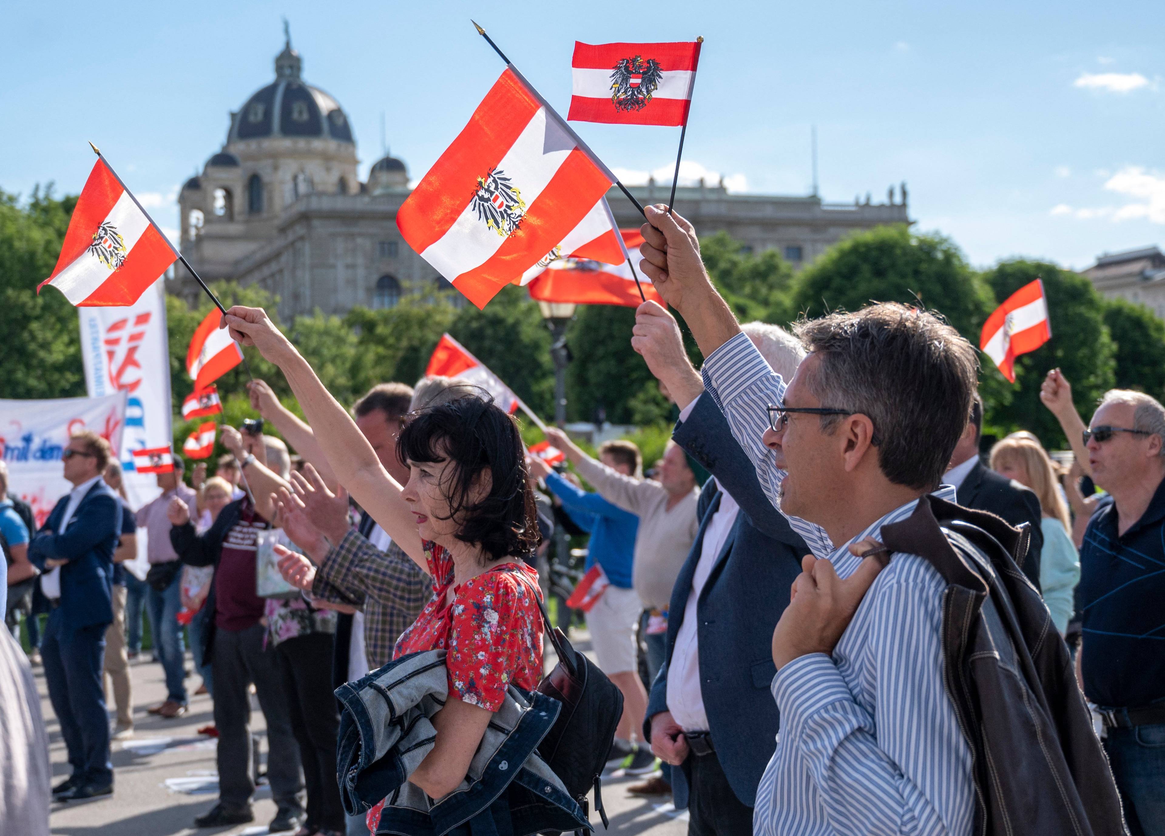 Zwolennicy FPÖ demonstrują, trzymają w wyciągniętych do góry prawych rękach austriackie flagi