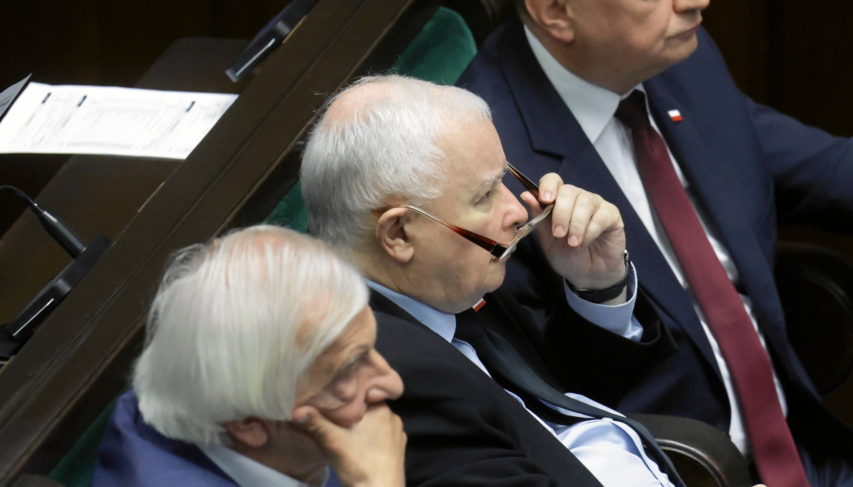 Jarosław Kaczyński na sali sejmowej patrzy na coś z ponad okularów