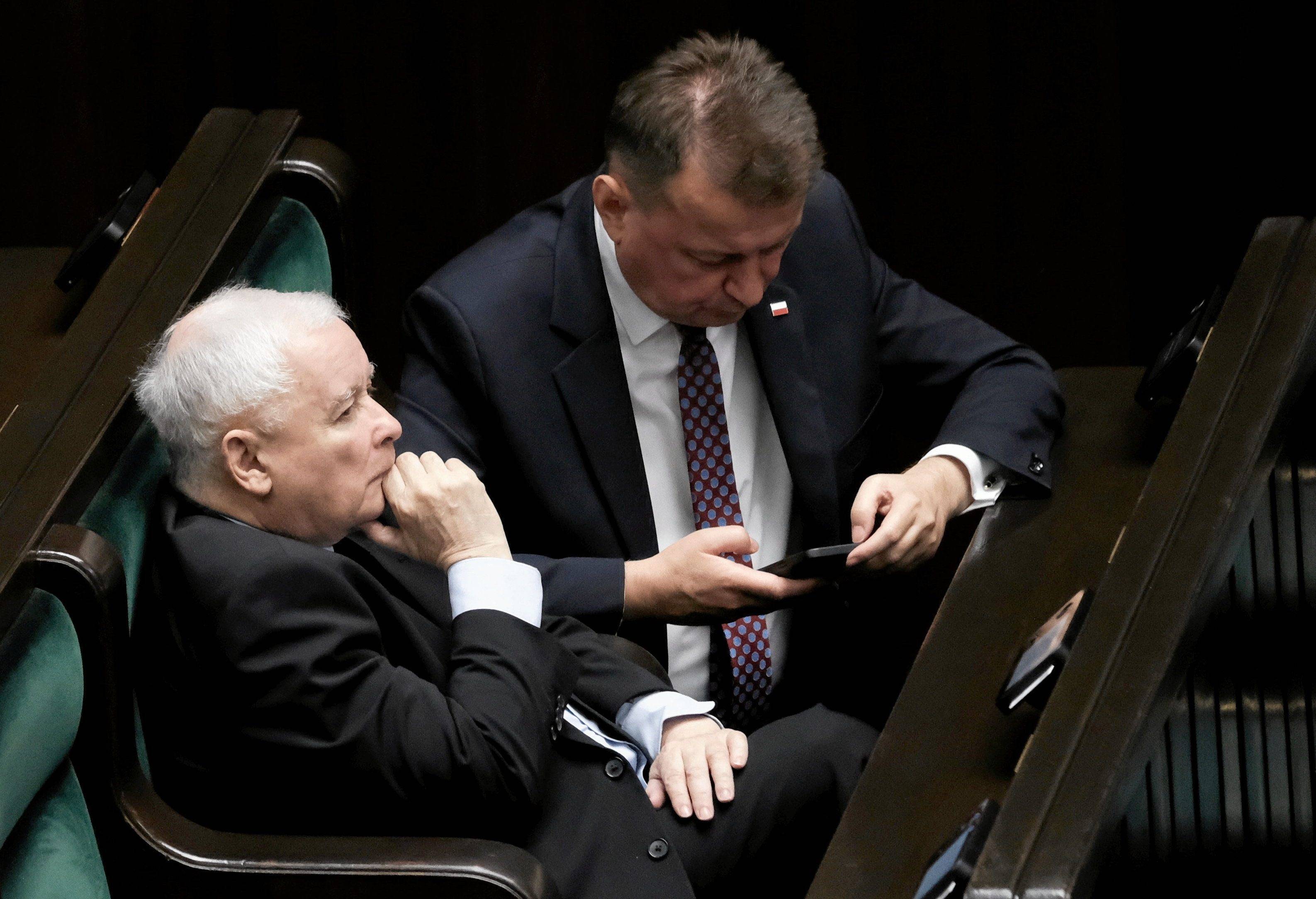 Jarosław Kaczyński siedzi w ławach poselskich w Sejmie, obok Marius Błaszczak patrzy w ekran telefonu.