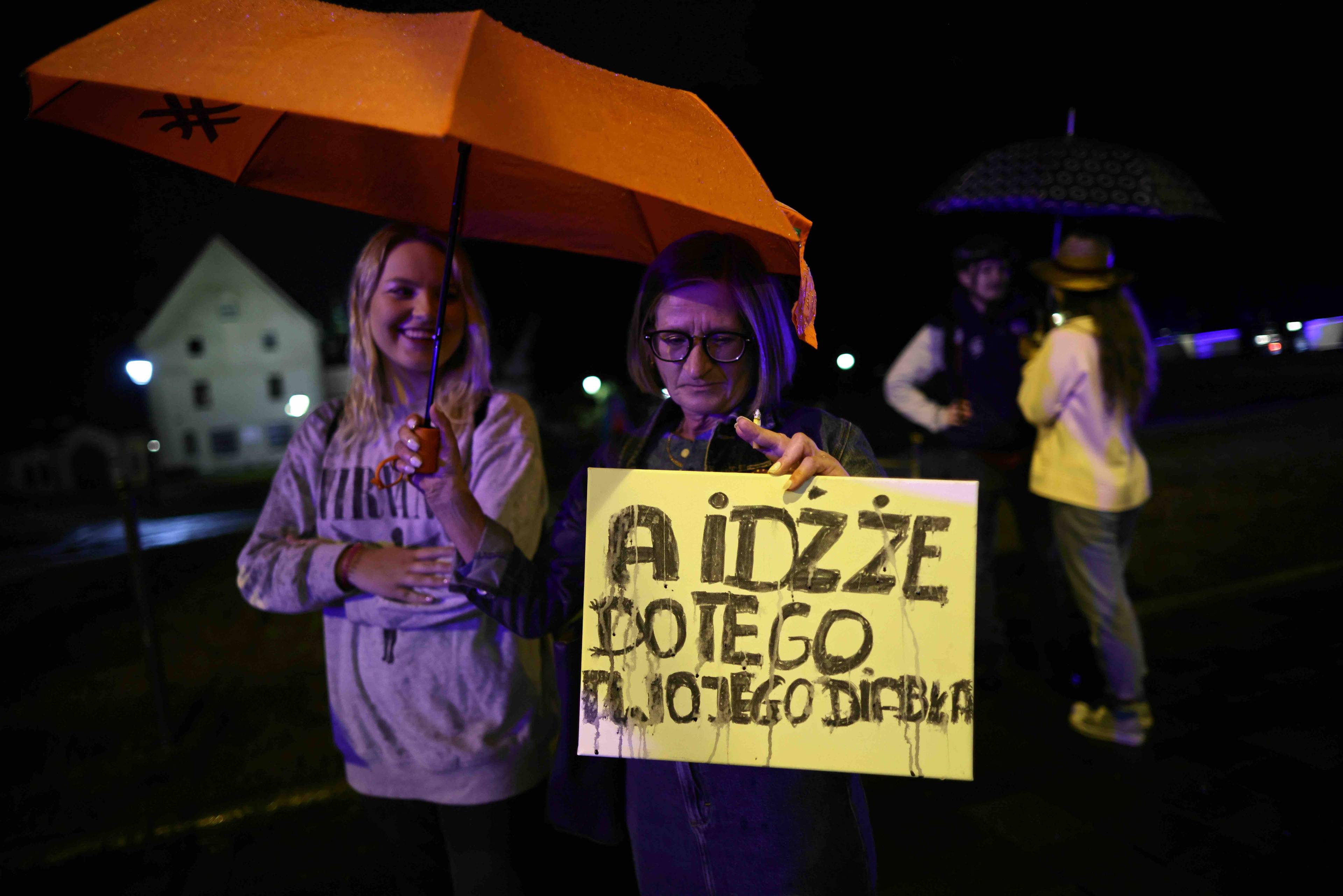 Kobieta i mężczyzna stoją przed siedzibą kurii w Krakowie trzymając plakat z napisem {A idźże do tego twojego diabła”. Abp Jędraszewski