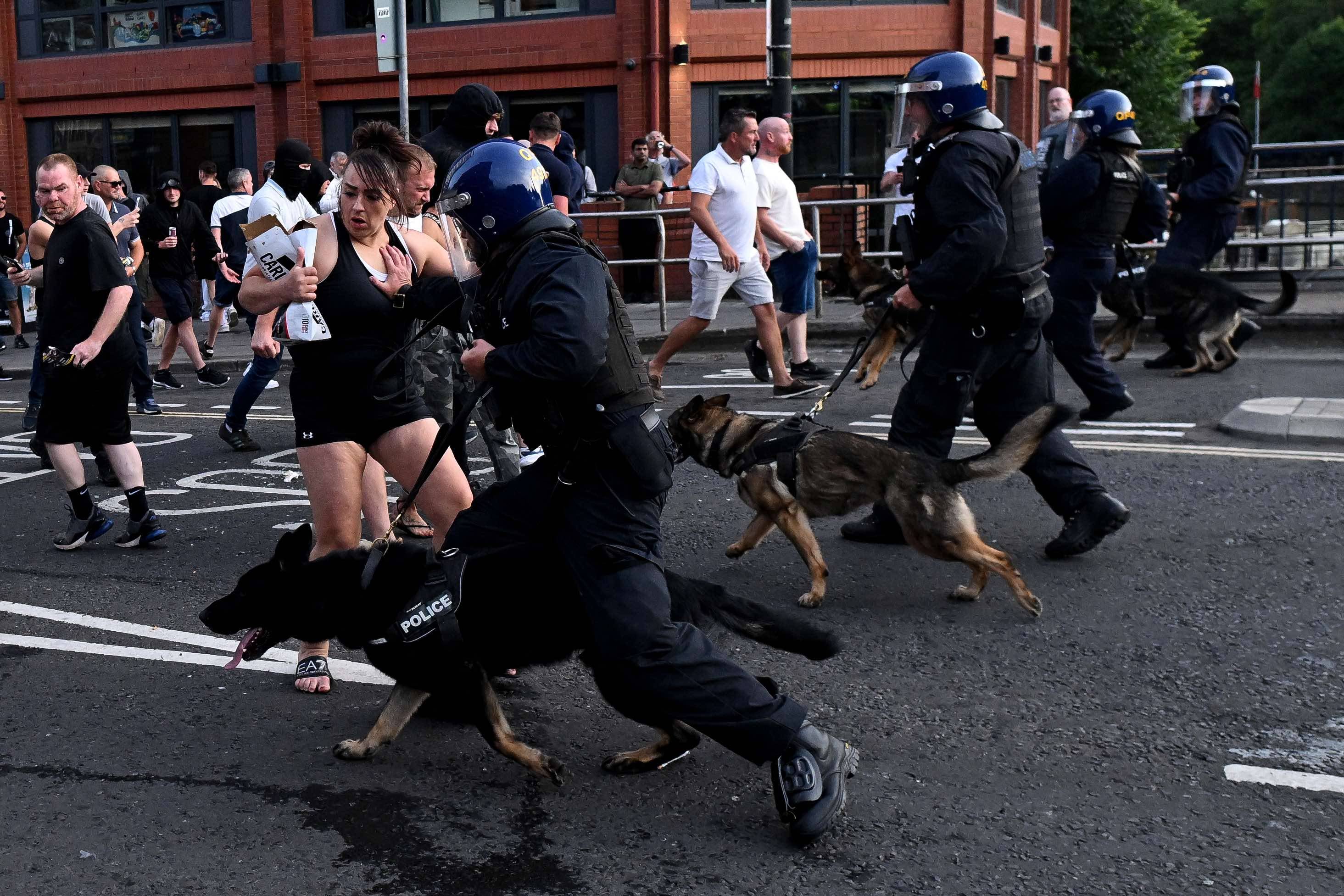 Policjanci z psami biegną w stronę demonstrantów na ulicy. Wielka Brytania