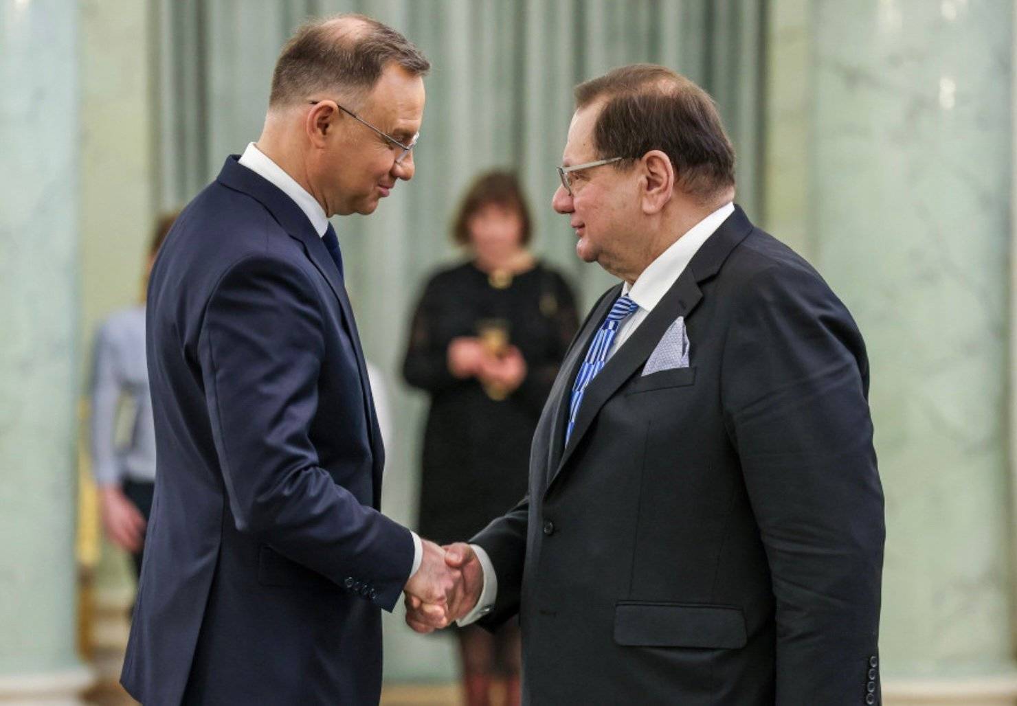 Szczupły mężczyzna (prezydent Duda) ściska dłoń korpulentnemu (poseł Kalisz), obaj w eleganckich garniturach