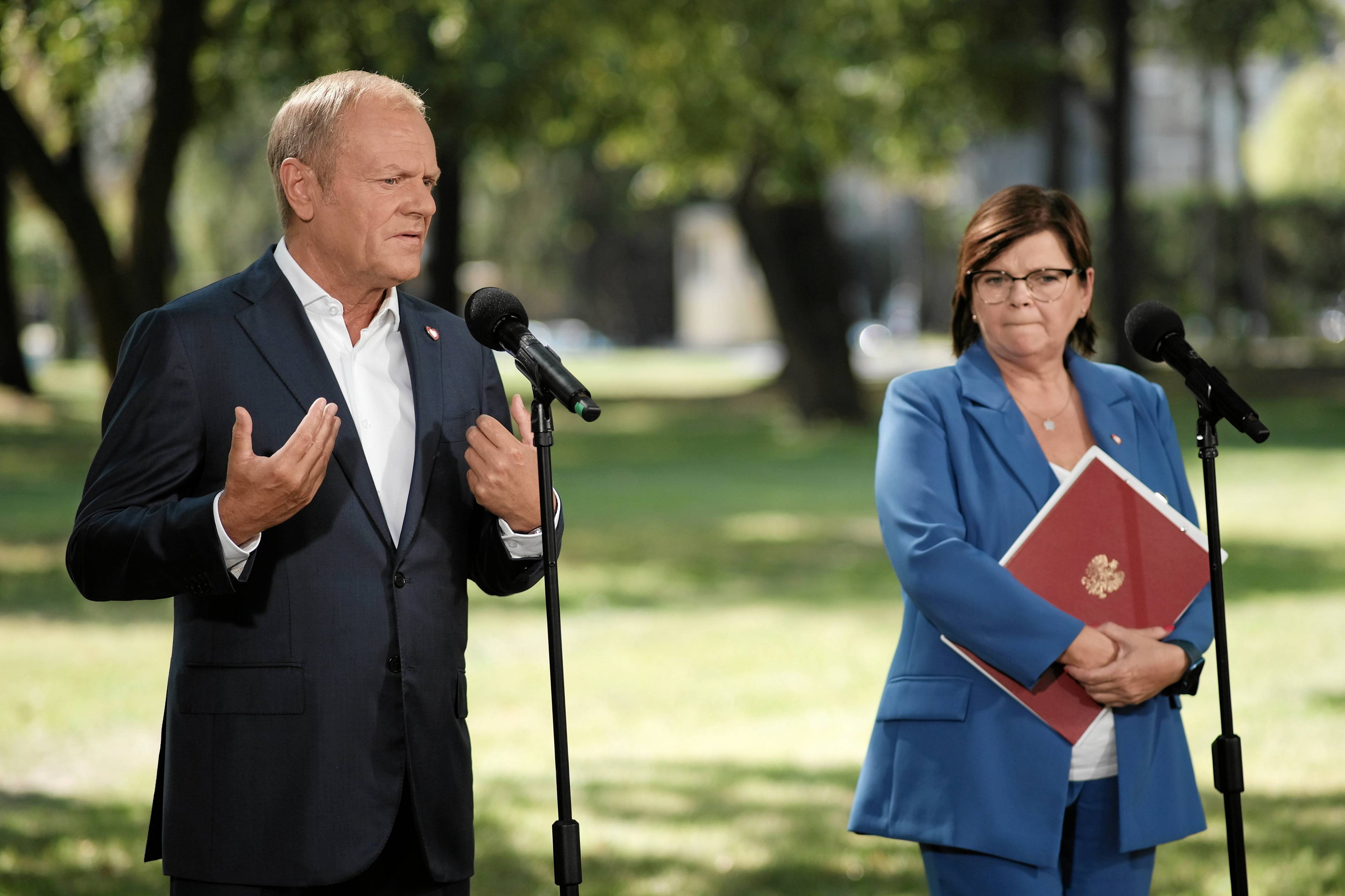 Donald Tusk i Izabela Leszczyna podczas konferencji. W tle trawnik i drzewa