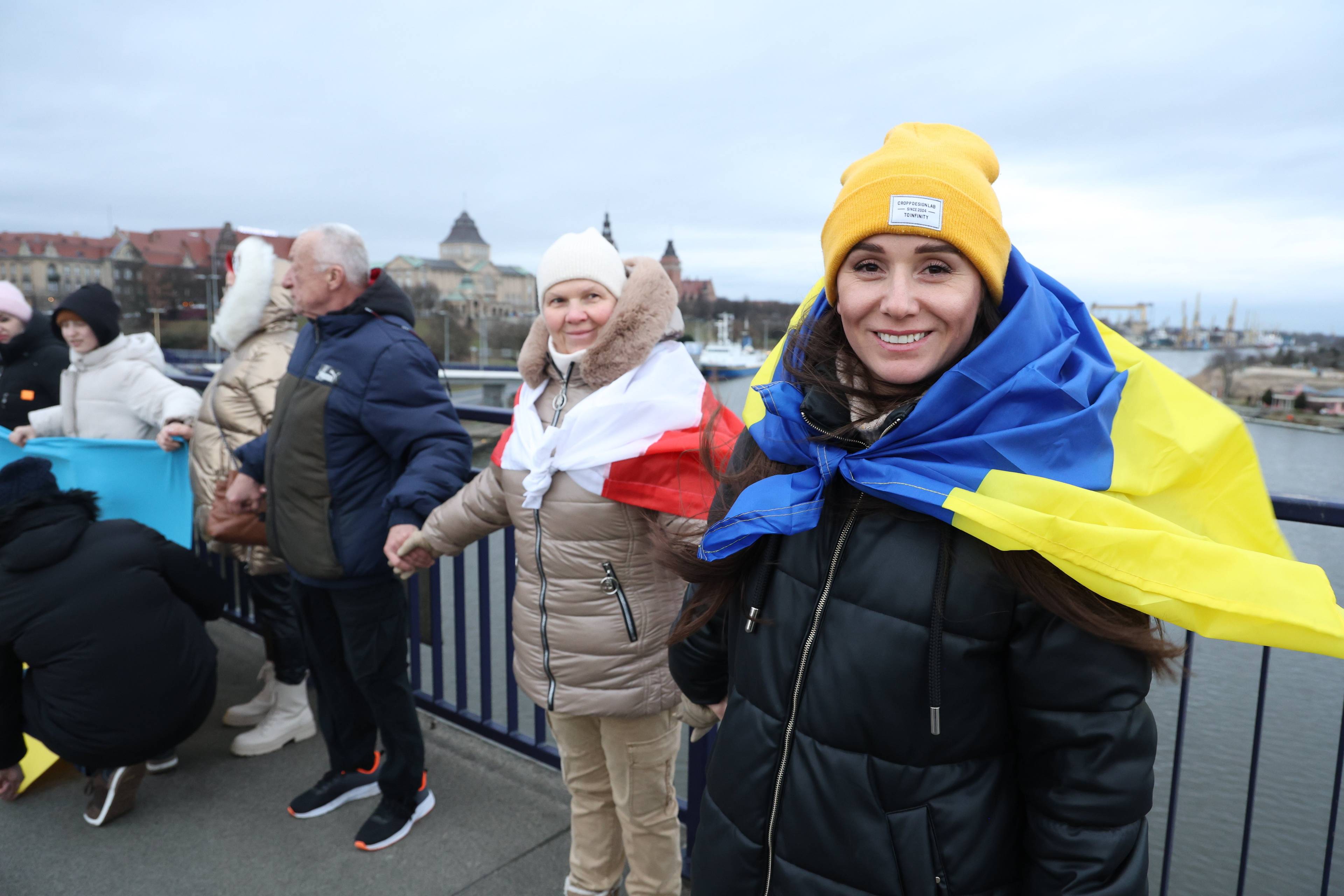 Ludzie owinięci we flagi Ukrainy i Polski trzymają się za ręce