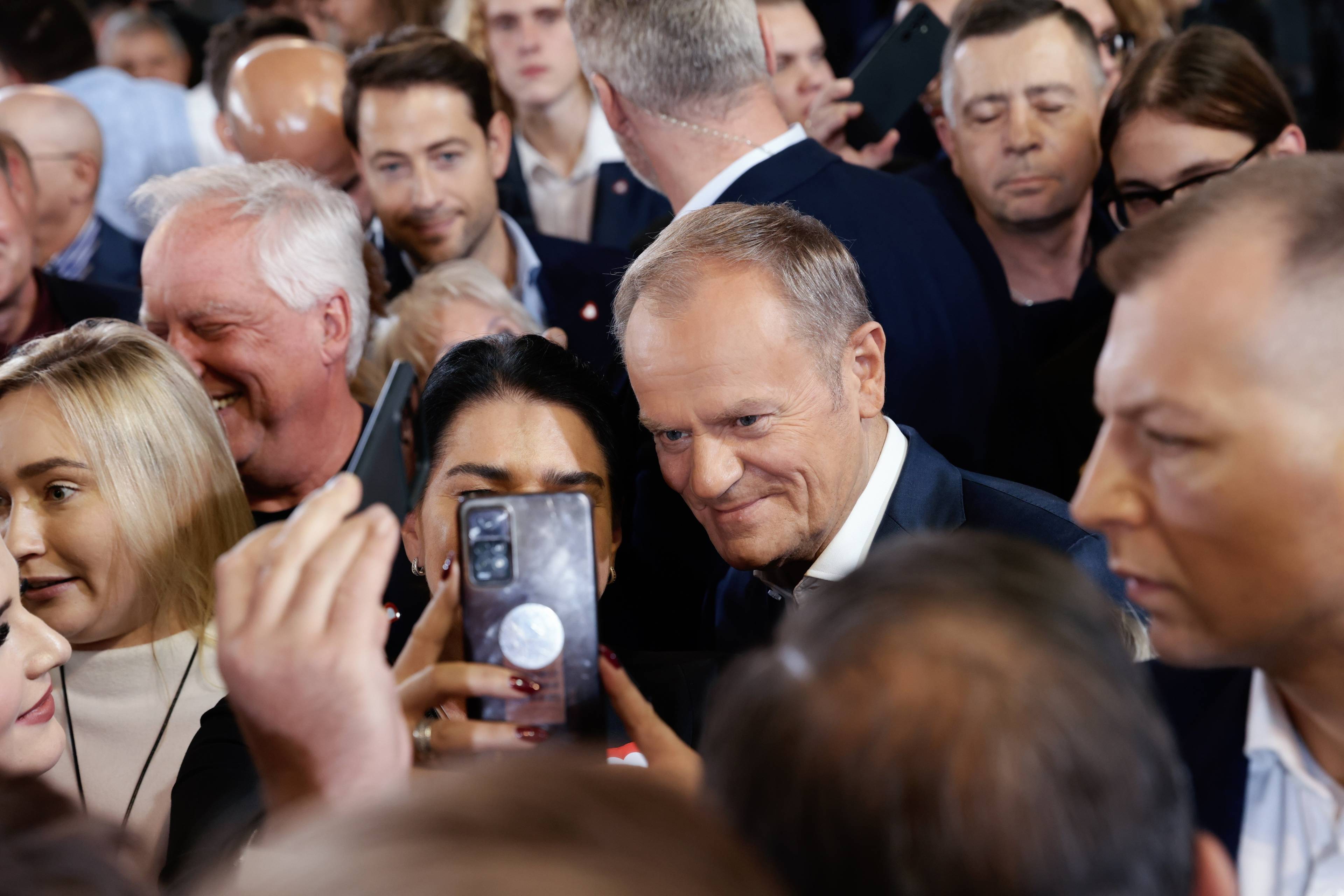 Donald Tusk w otoczeniu zwolenników robi sobie z nimi selfie komórką