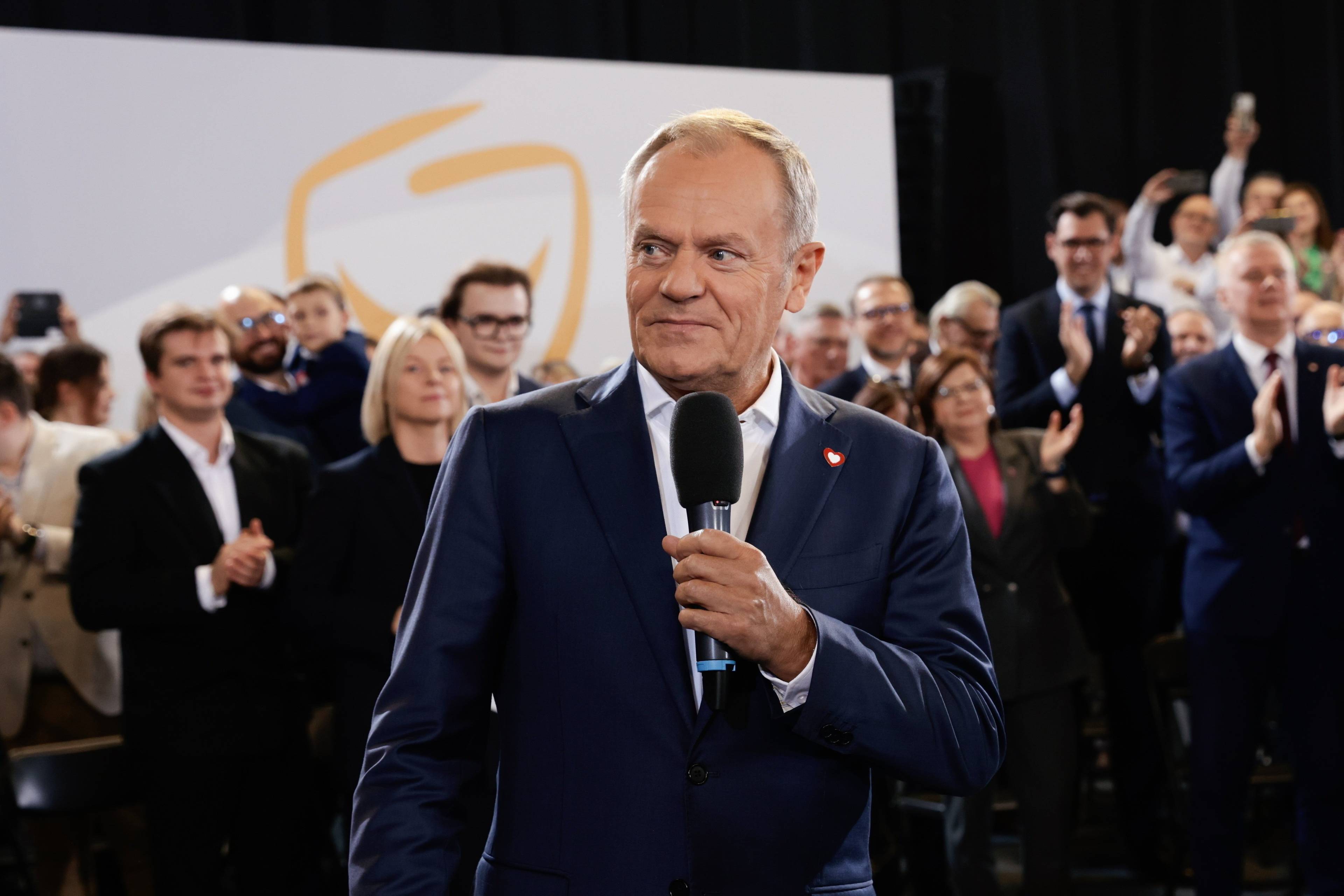 Donald Tusk trzymając mikrofon przemawia do członków partii