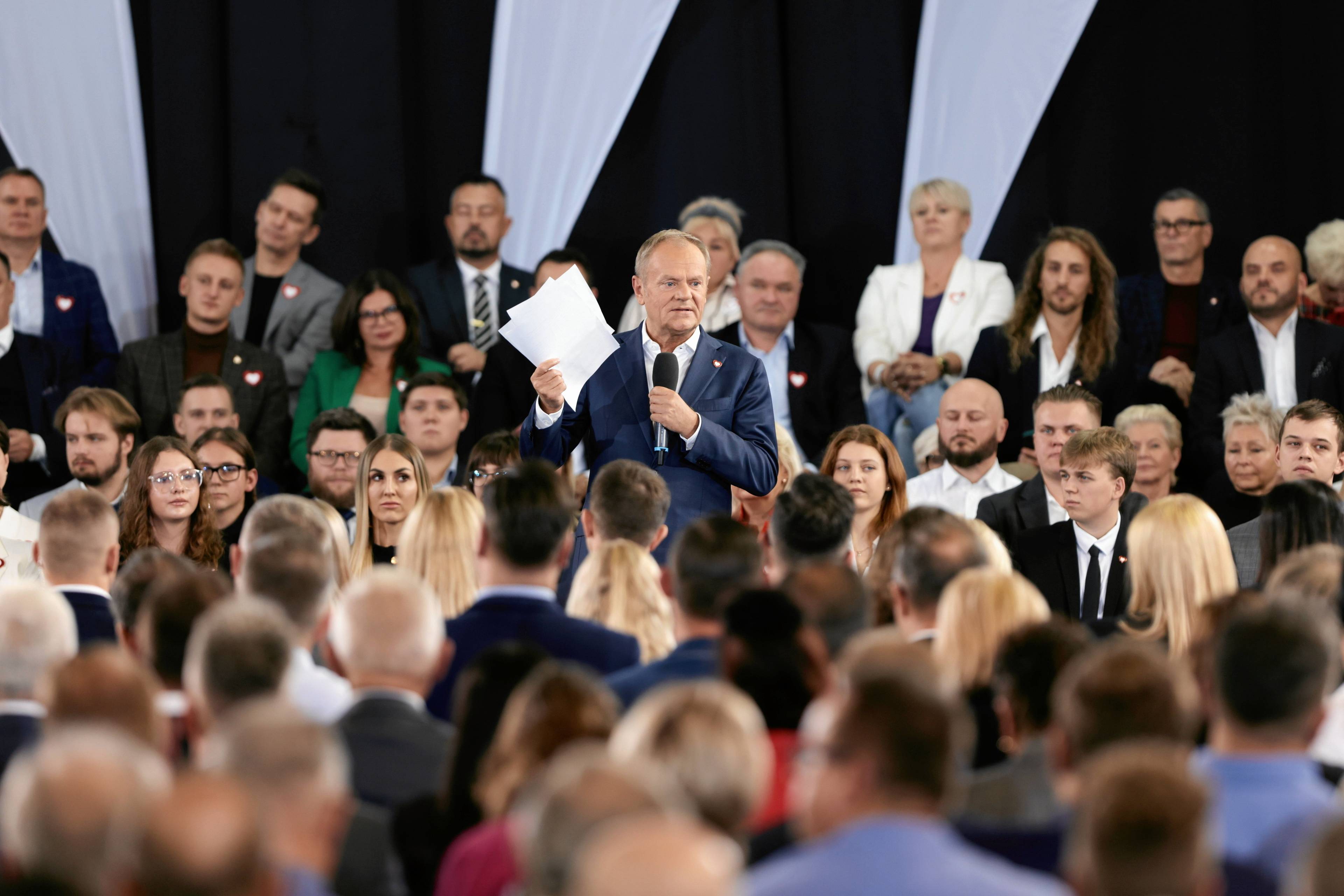 Donald Tusk otoczony uczestnikami partyjnej konwencji pokazuje plik papierów