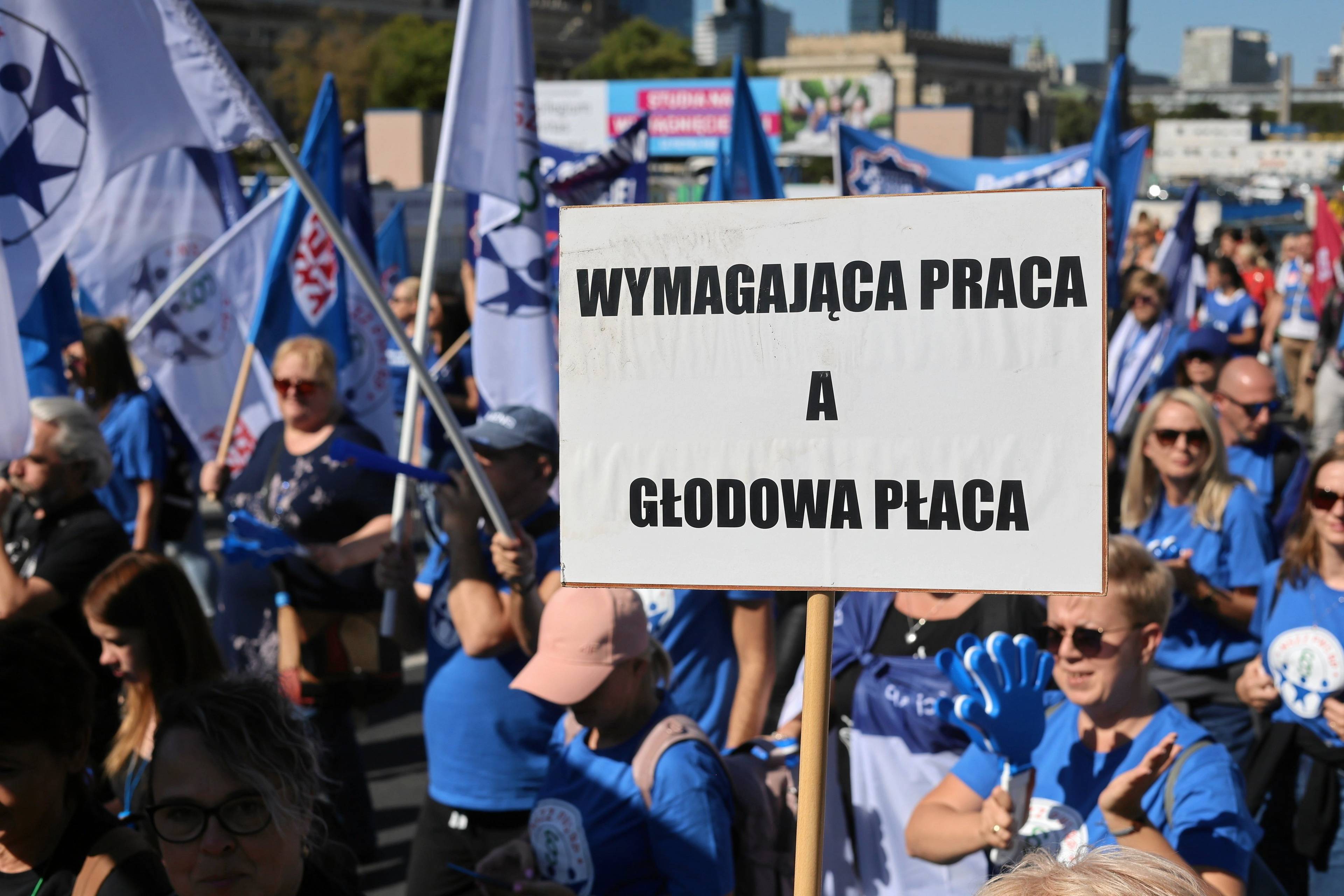 Protest związkowców. Na pierwszym planie transparent "WYmagająca praca a głodowa płaca"