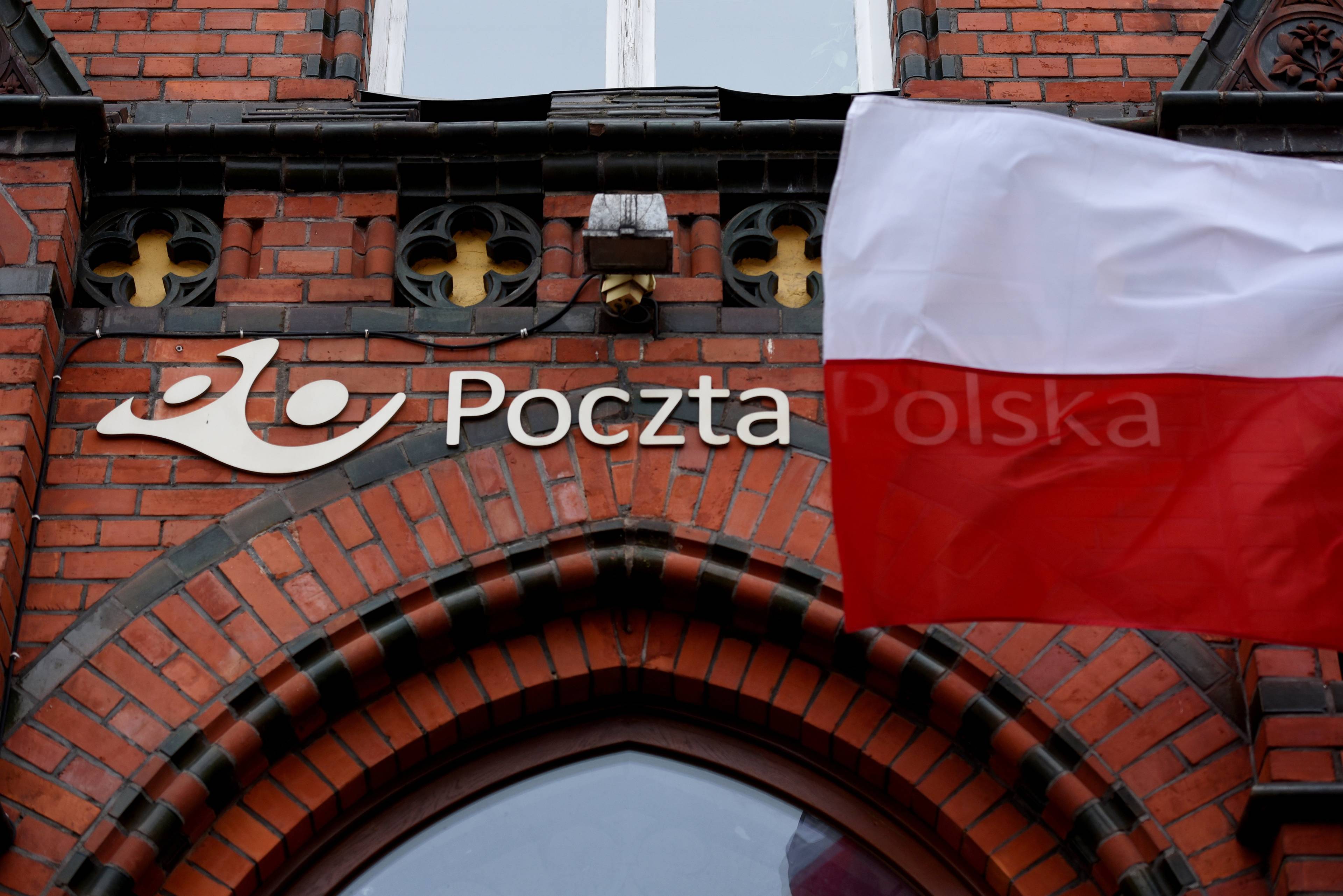 Ceglany budynek poczty, logo i napis poczta, powiewająca biało-czerwona flaga