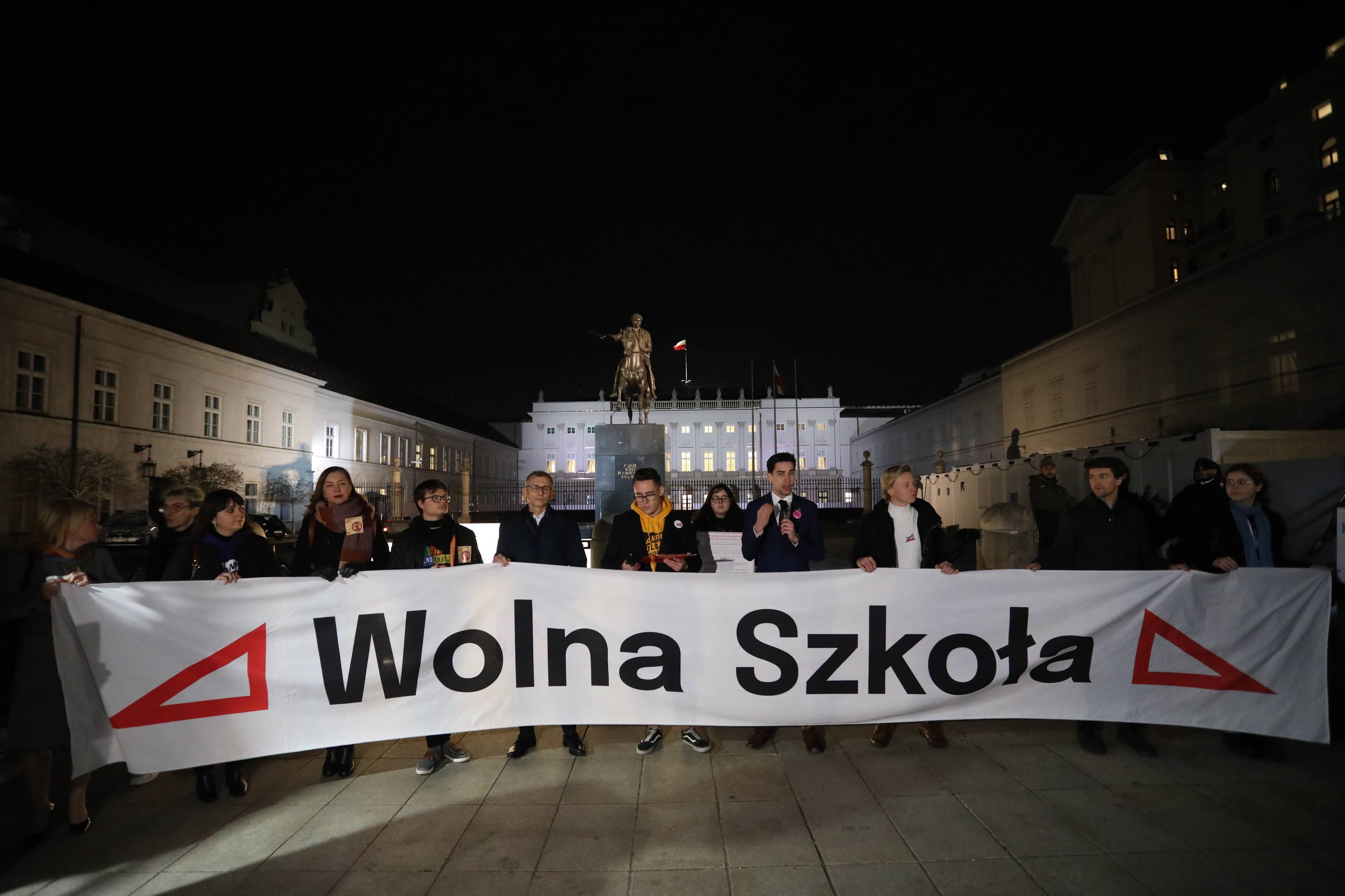 Ludzie przed Pałacem Prezydenckim w Warszawie stoją z transparentem "Wolna szkoła" i znakiem czerwonej ekierki symbolizującym protest