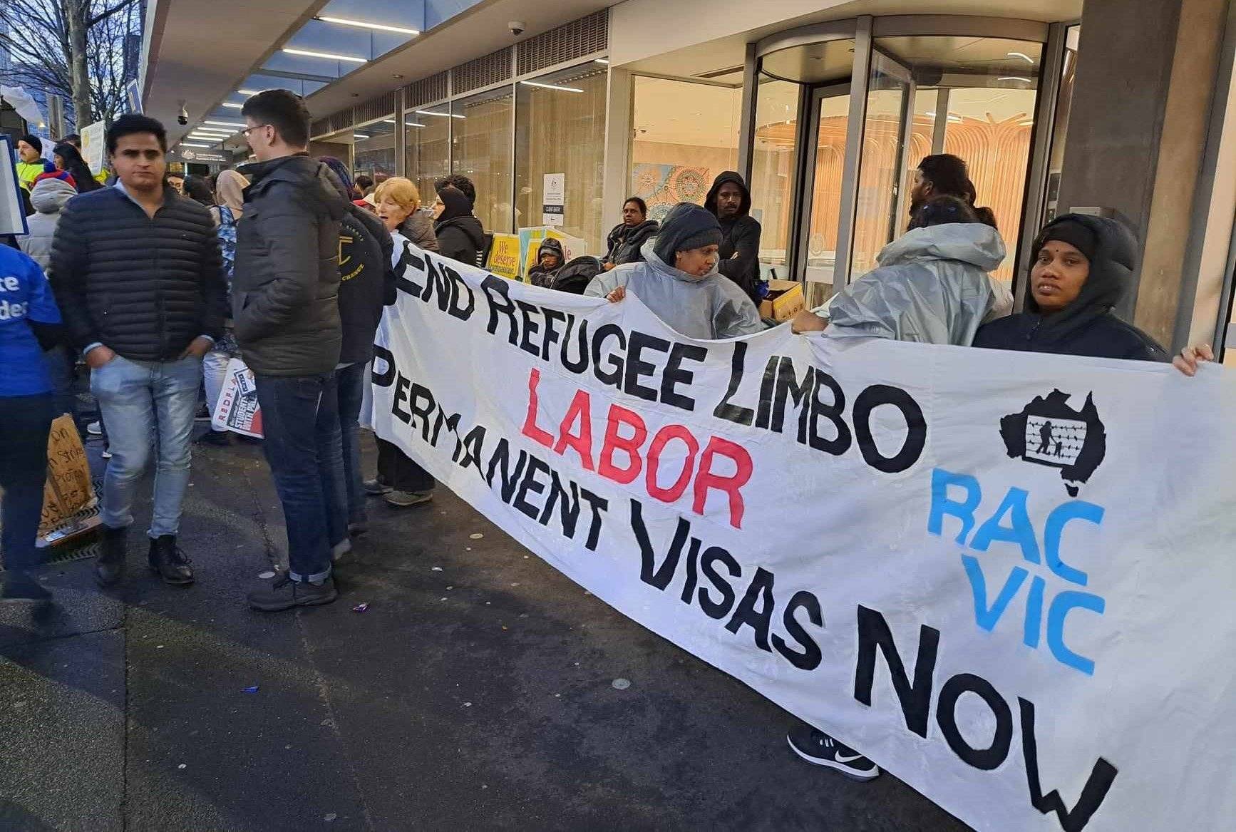 Protestujący ludzie trzymają długi biały baner z hasłami po angielsku.