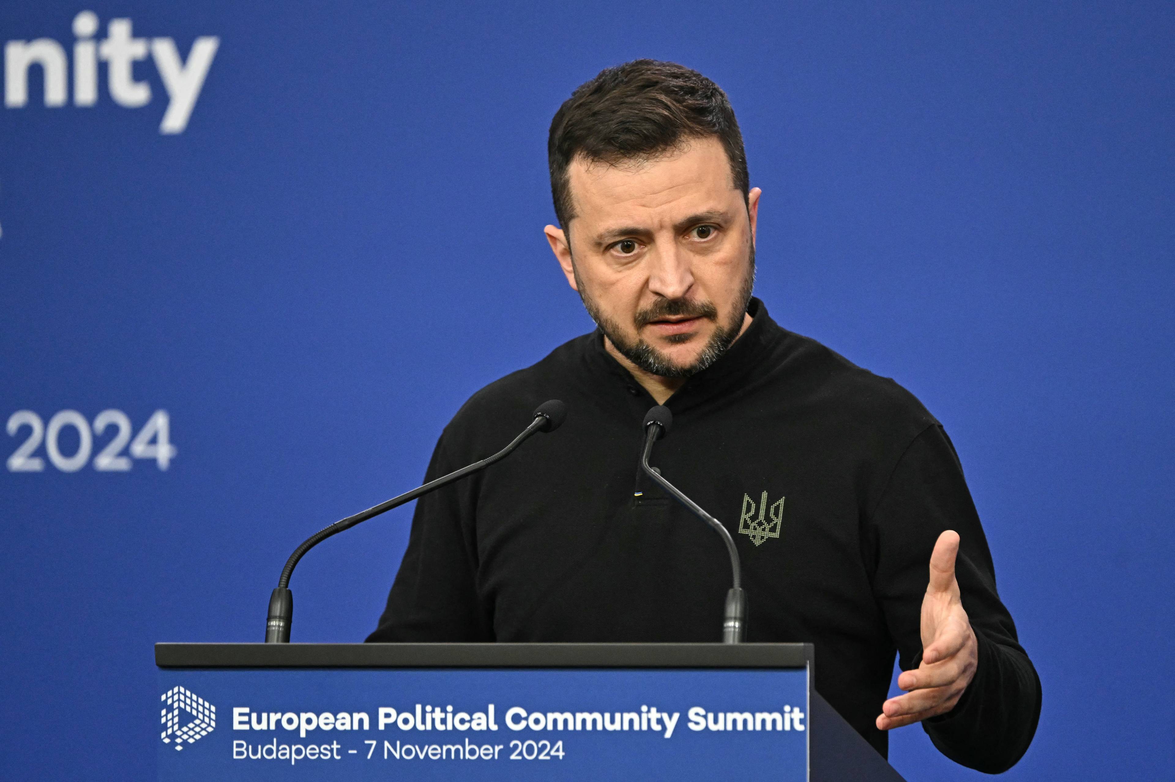 Na zdjęciu jest mężczyzna ok. 45 lat. Ma czarne krótkie włosy i brodę. Jest ubrany w czarną bluzę z wyhaftowanym tryzubem po prawej stronie. Przemiawia przez mikrofony.