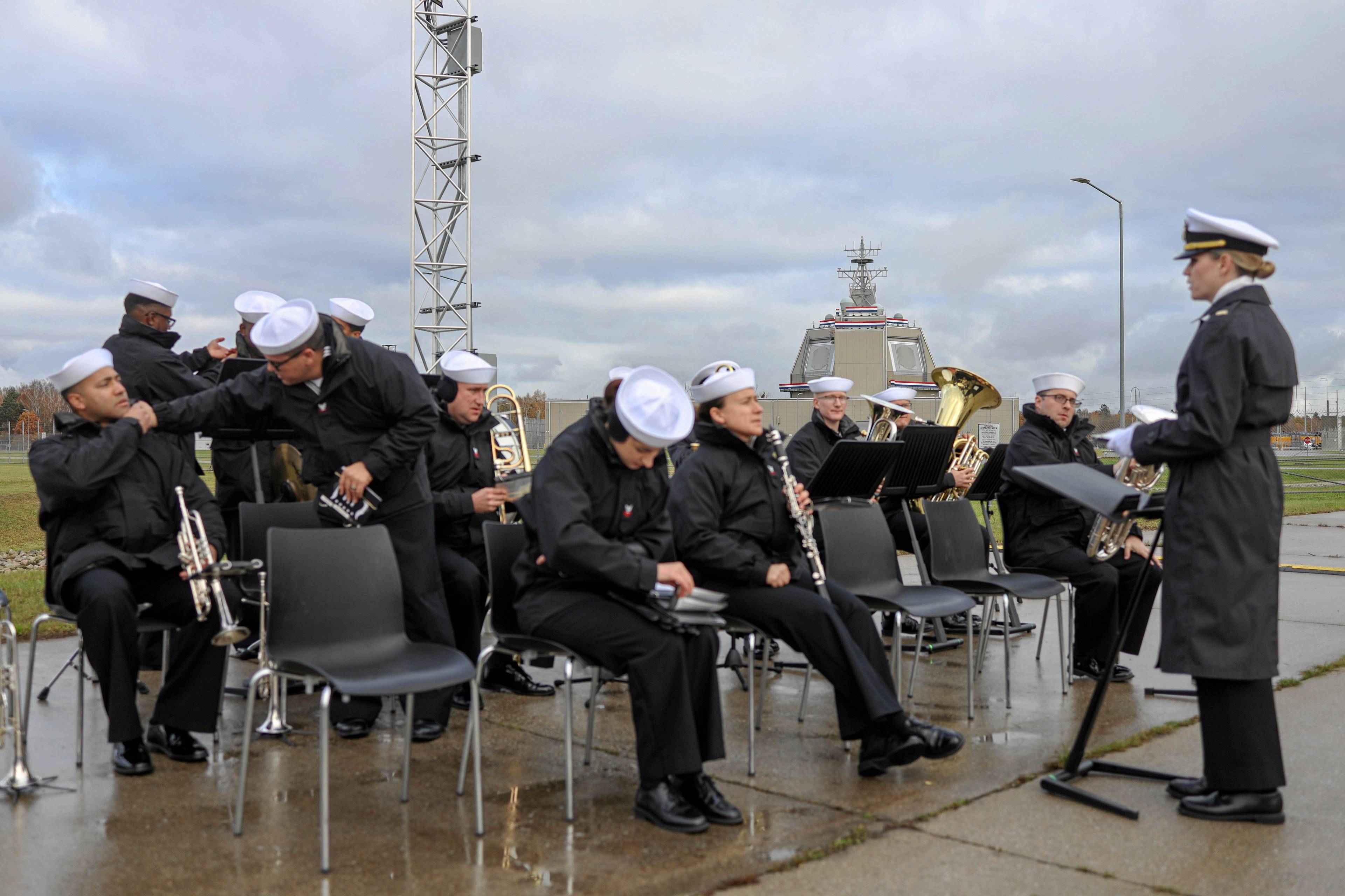 Orkiestra na płycie lotniska. W tle budynek przypominający mostek kapitański