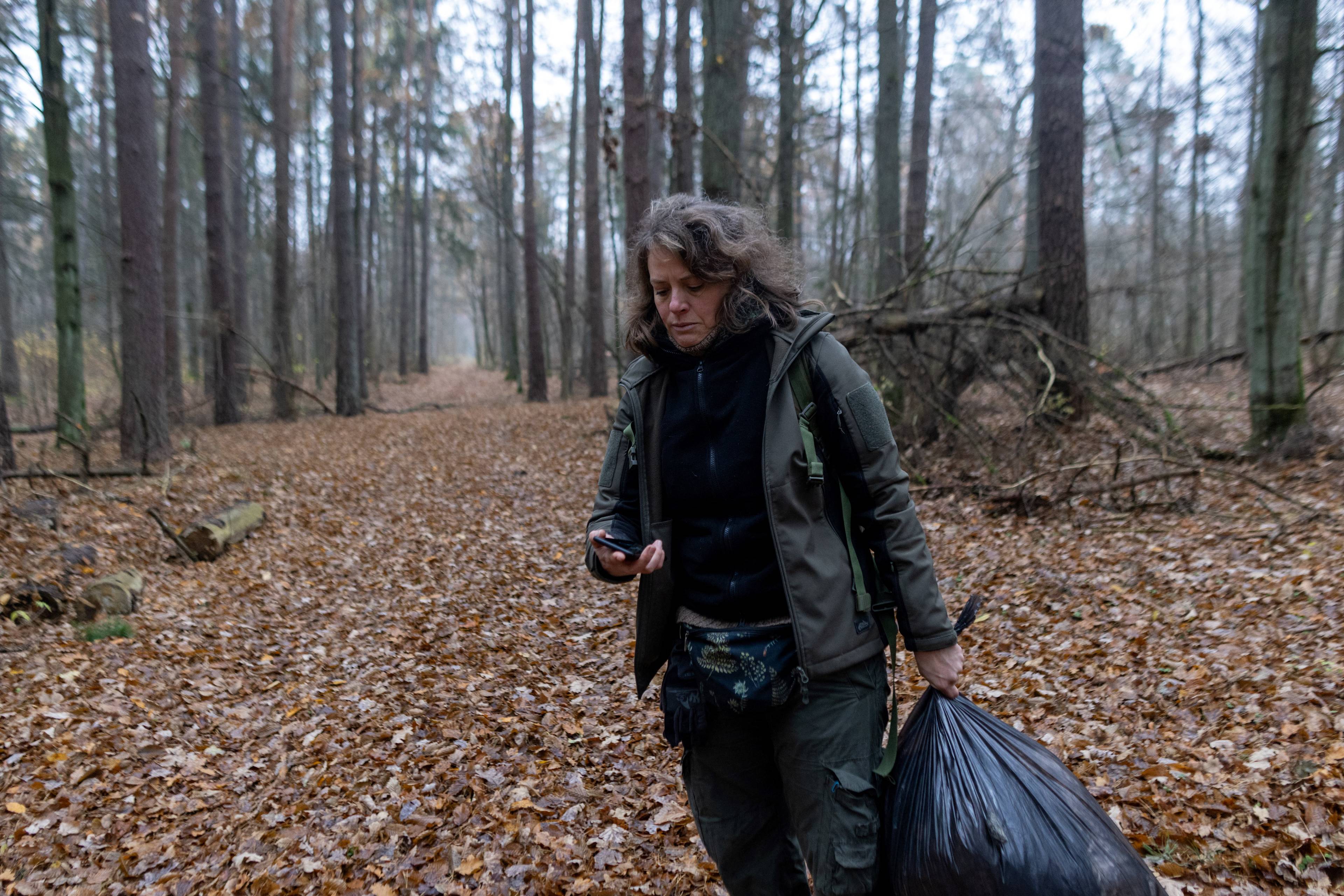 Kobieta patrzy w komórkę, stoi na leśnej drodze