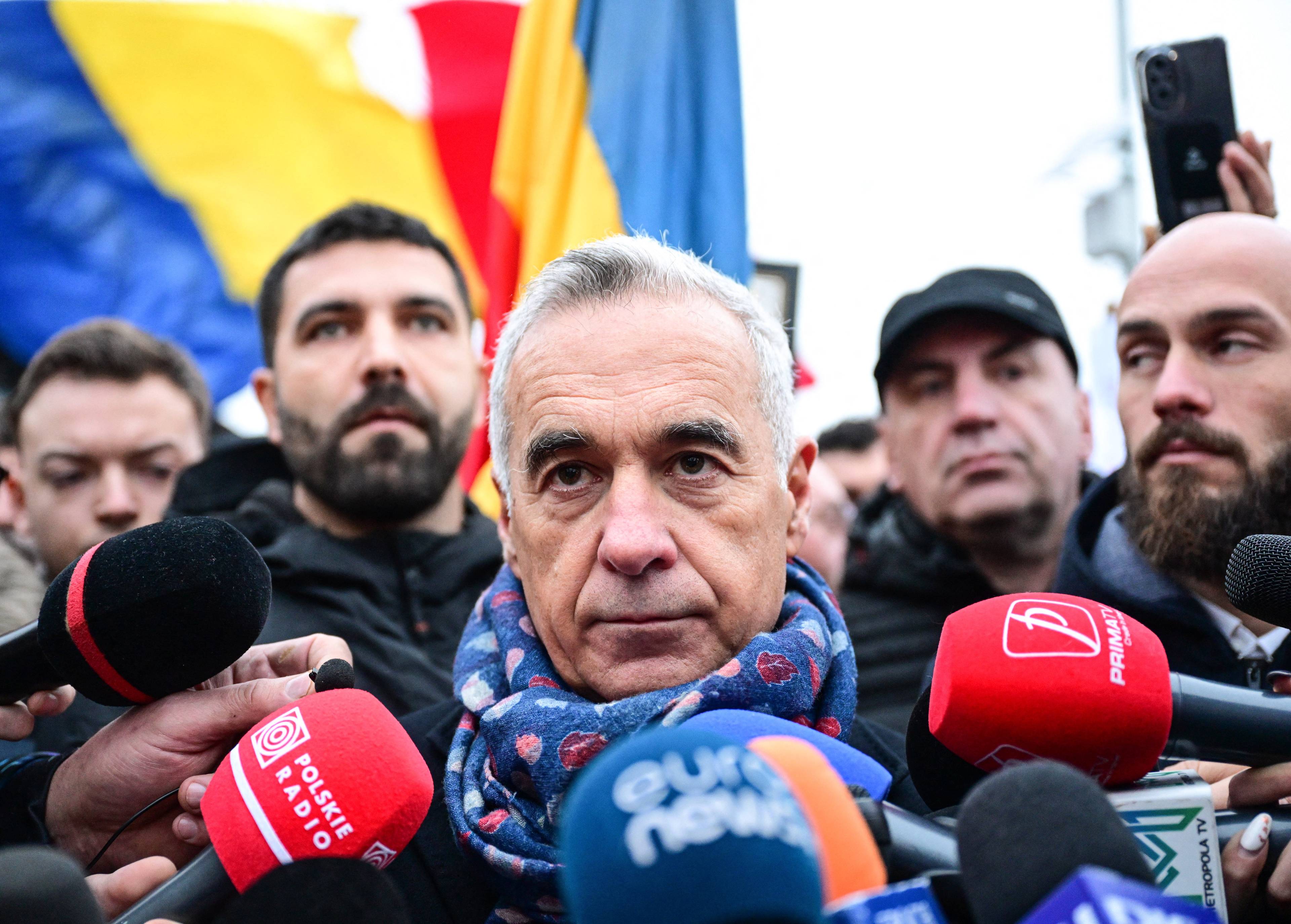 Siwy mężczyzna w szaliku w gąszczu mikrofonów