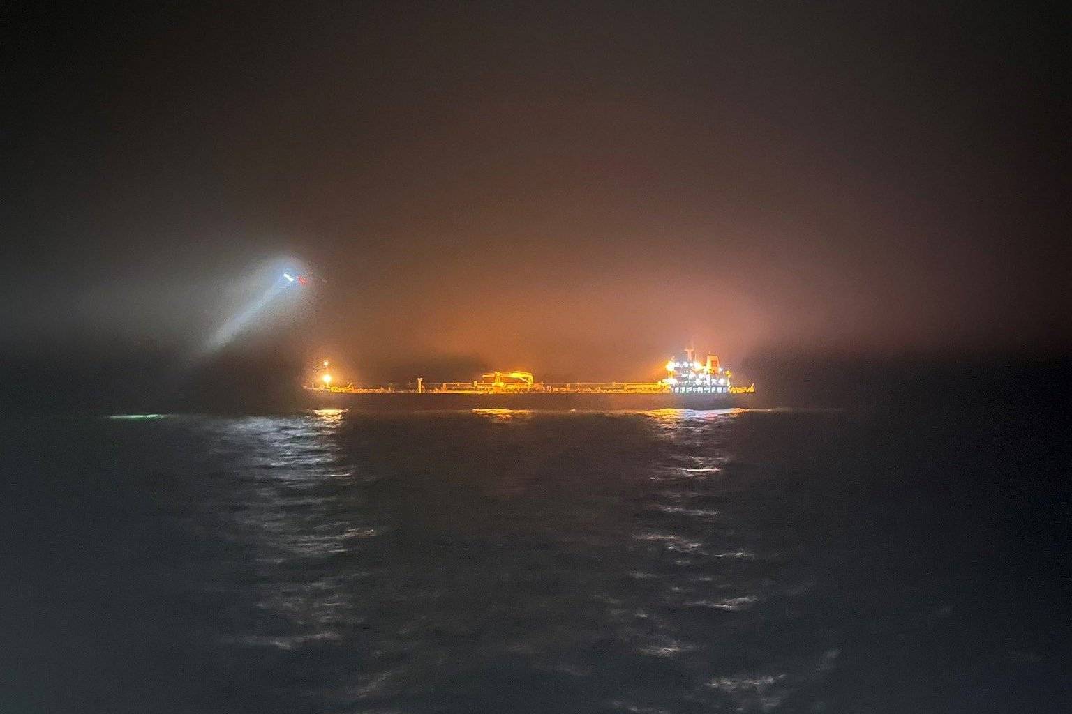 Nocne zdjęcie z oddali - widać oświetlony reflektorami statek na morzu