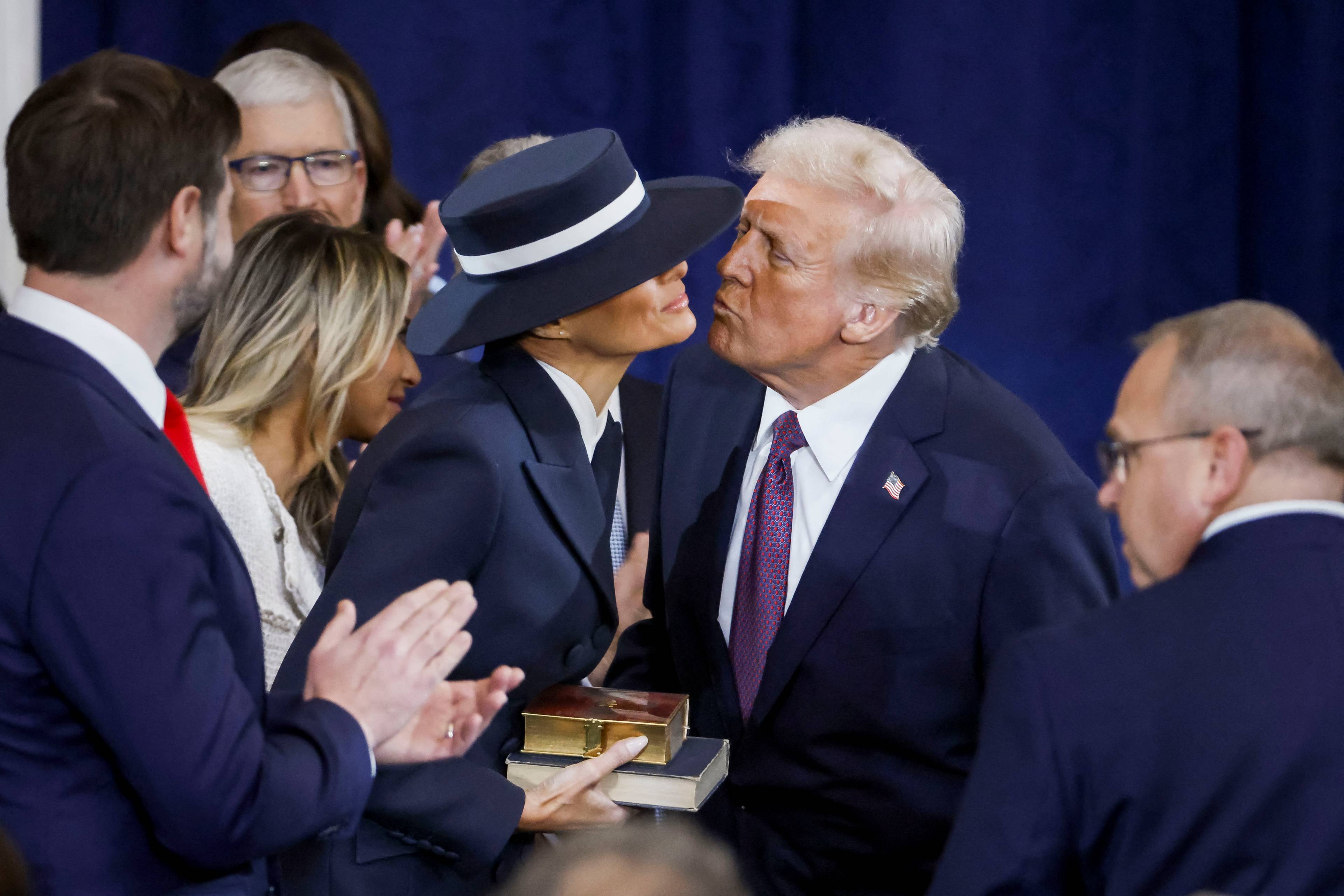 Donald Trump nachyla się, by pocałować żonę, wokół nich oficjele, żona Trumpa nosi bardzo duży kapelusz