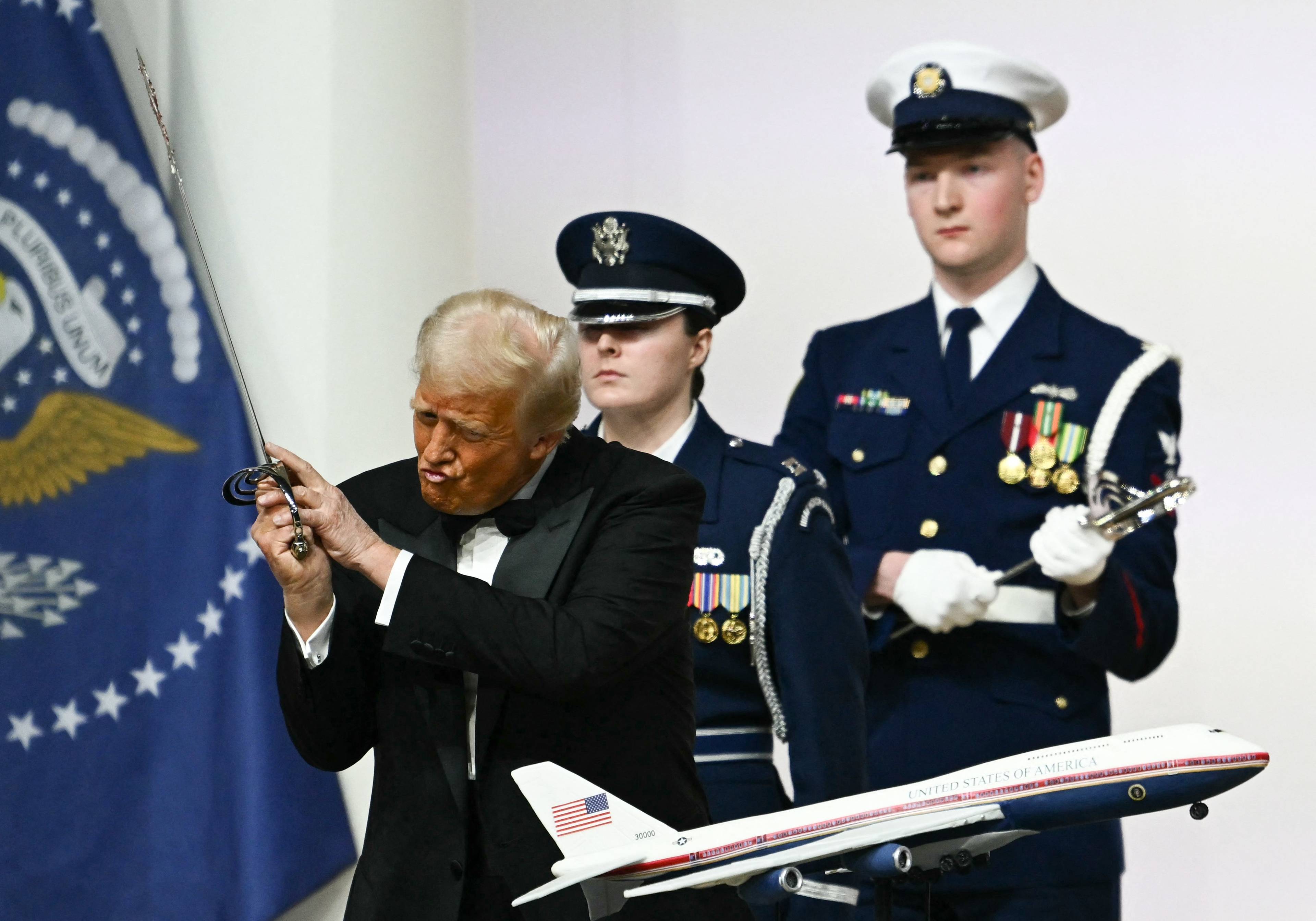 Donald Trump wymachuje szablą nad tortem w kształcie Air Force One, z tyłu żołnierze w galowych mundurach