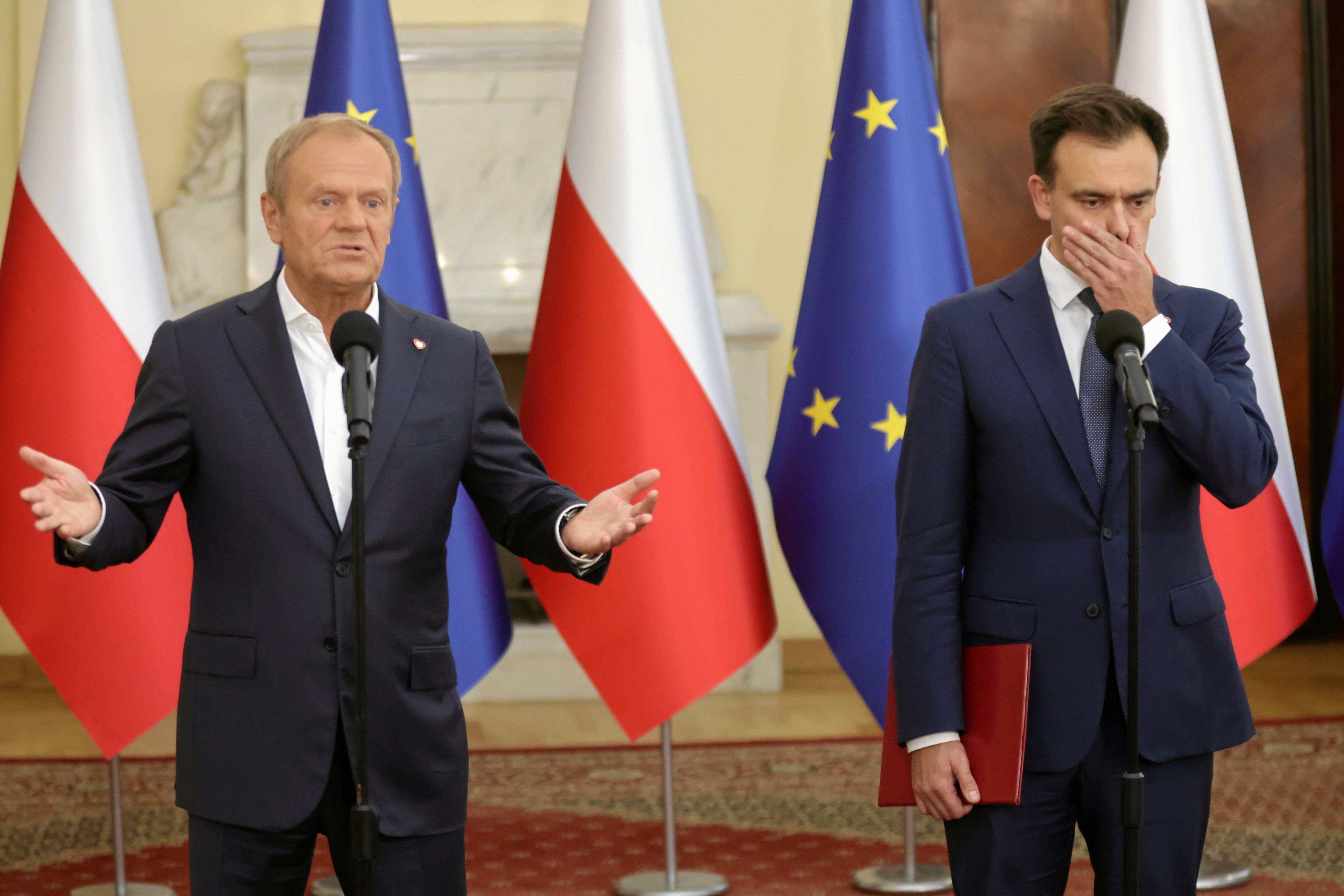 Obok siebie stoją premier Donald Tusk ( z rozłożonymi rękoma) i minister finansów Domanński (z zasłoniętymi ustami)