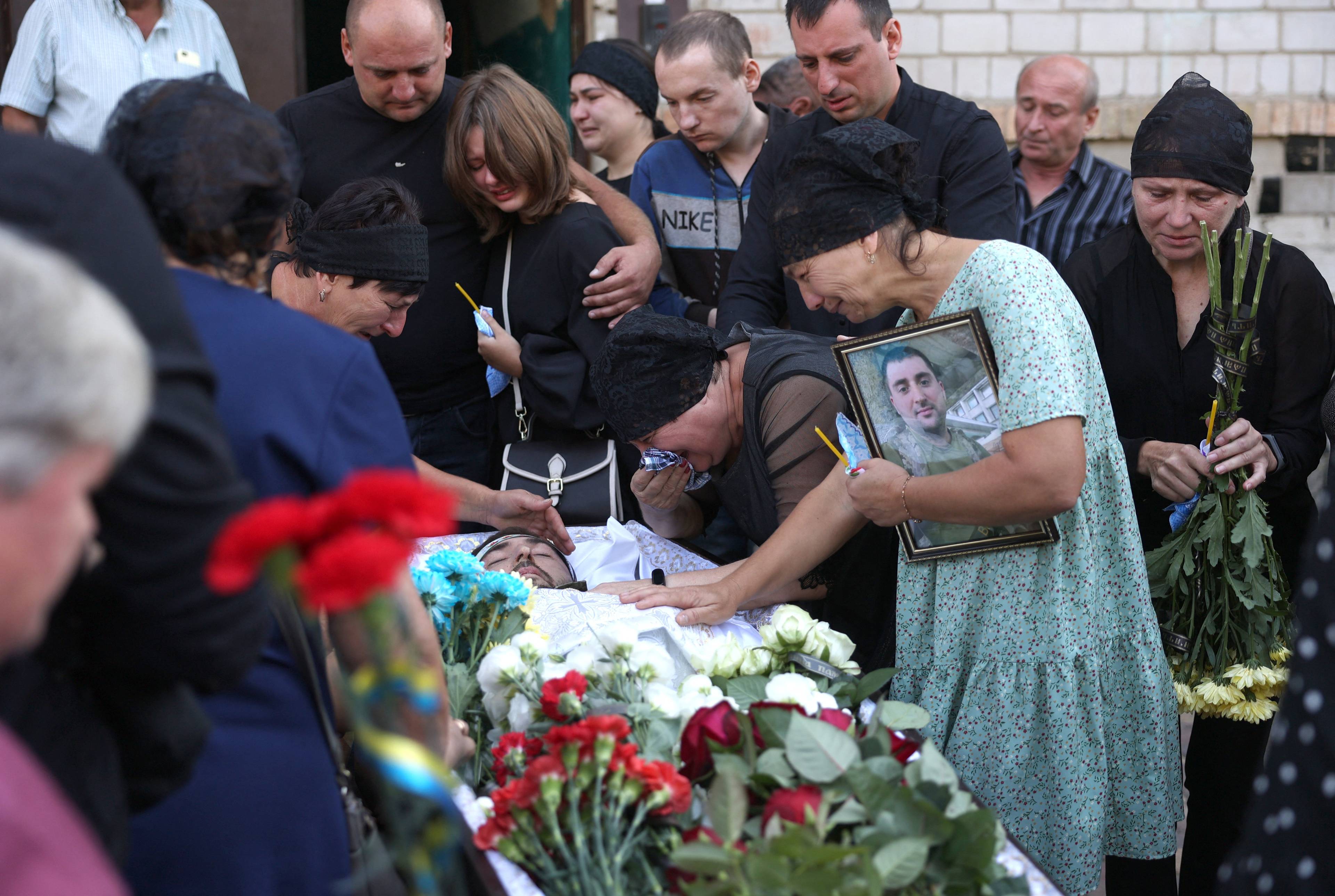 Rodzina żegna poległego żołnierza, ludzie płaczą nad trumną, przy niej widać kwiaty