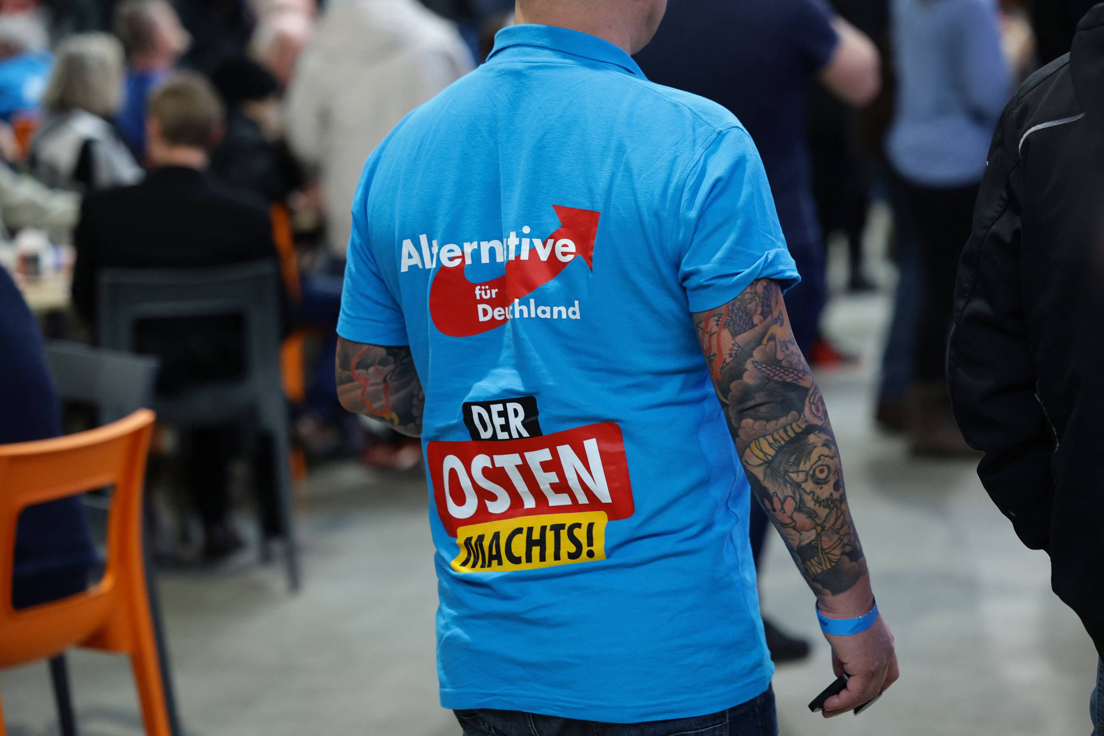 Mężczyzna w tatuażach w niebieskiej koszulce z napisem Alternative fur Deutschland