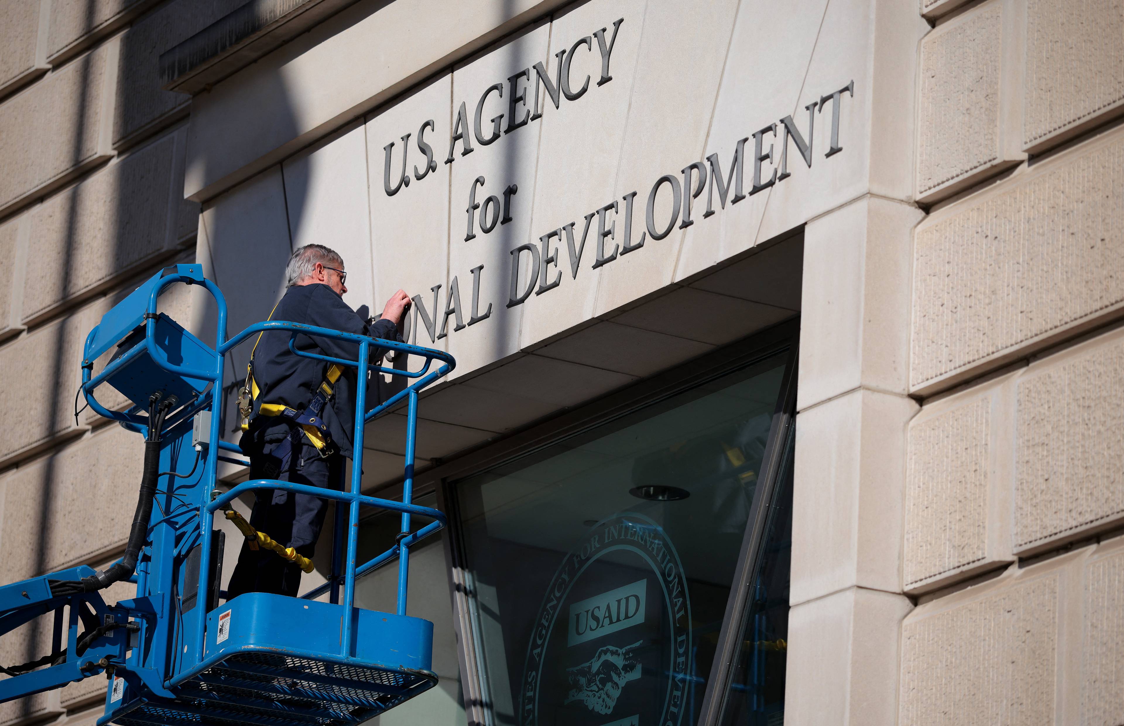 Robotnik na wysięgniku usuwa napis nad wejściem do USAID